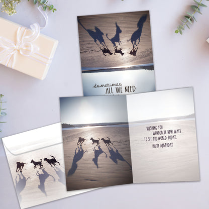 Front and inside view of a birthday card showcasing an upside-down image of dogs on a beach with a message about perspective, with a matching envelope.