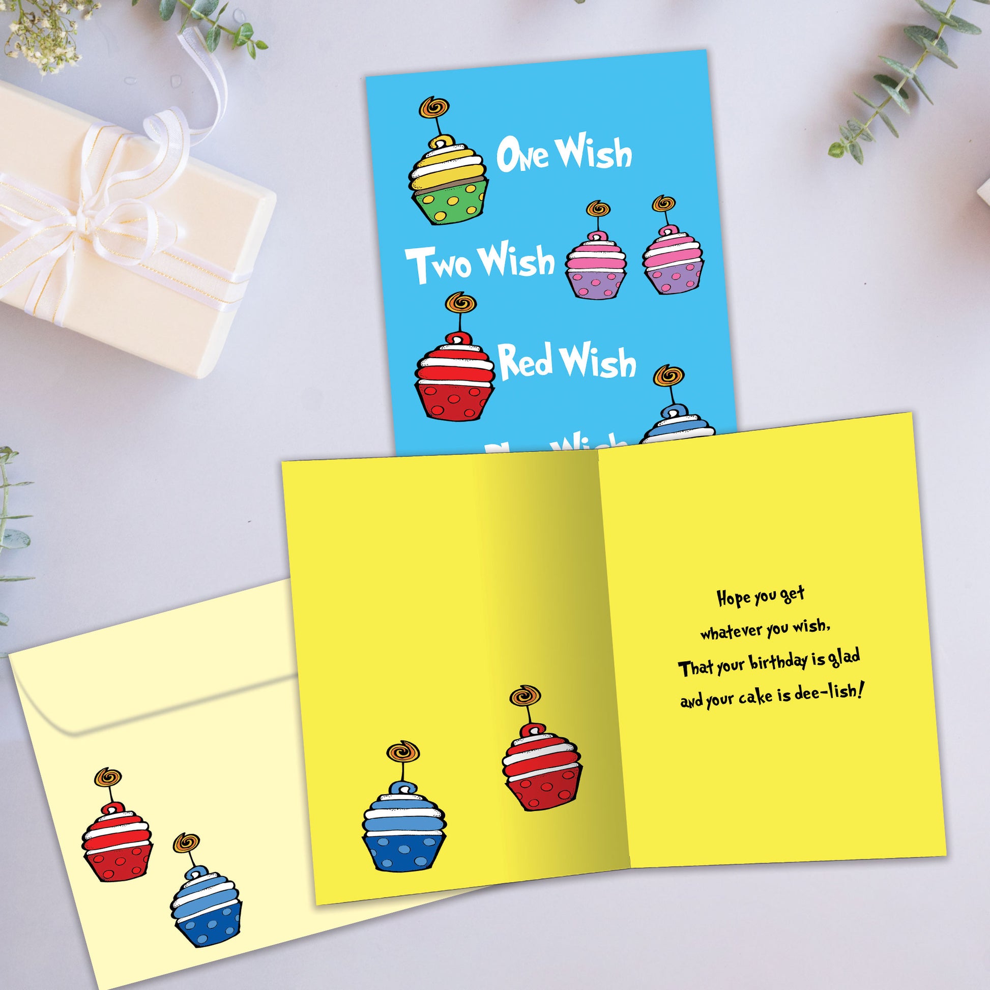 Front and inside view of a Birthday greeting card showcasing the message "one wish, two wish, red wish, blue wish" with primary-coloured cupcakes on a light blue background, with a matching envelope.