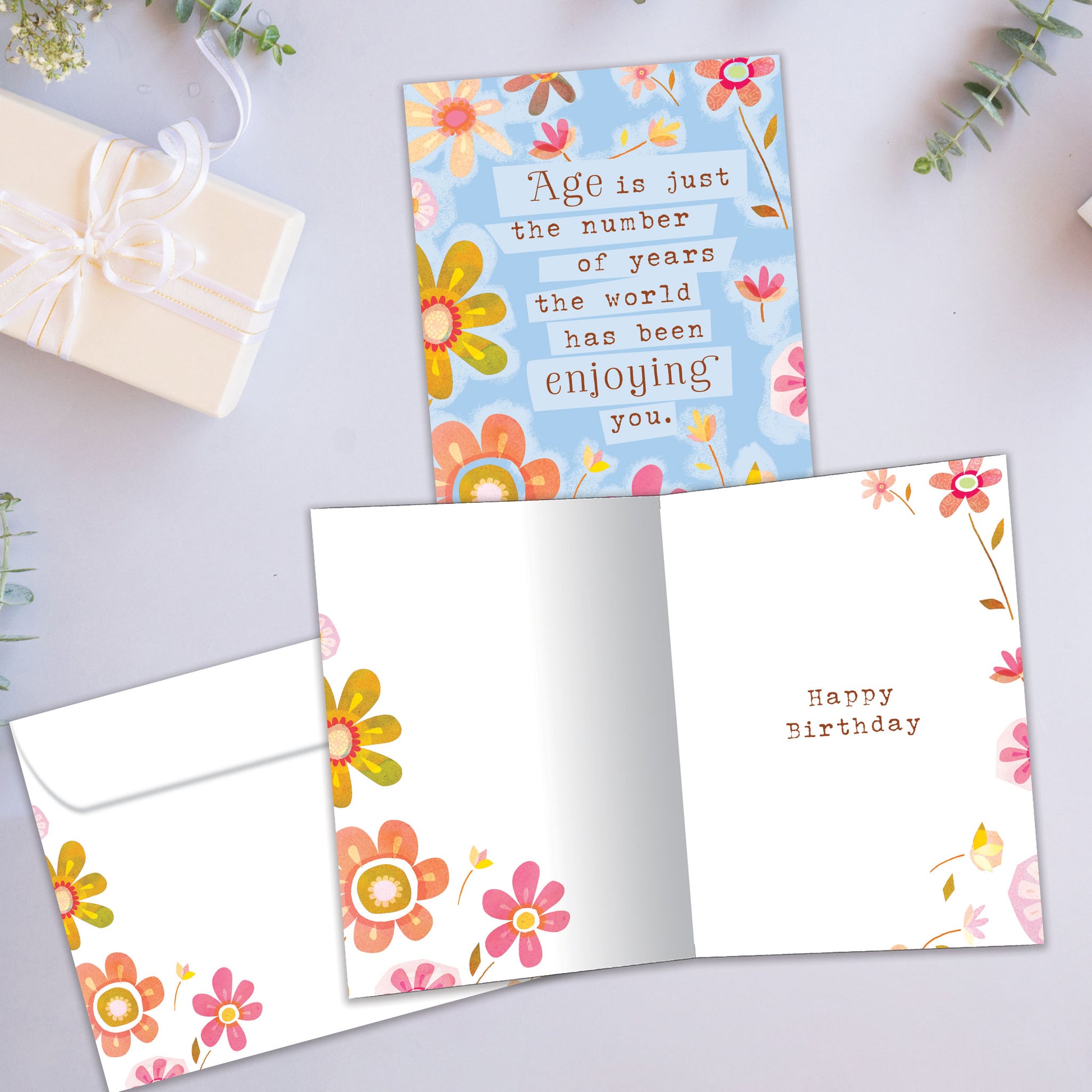 Front and inside view of a Birthday greeting card showcasing pastel-colored flowers surrounding a message about age being just a number, with a matching envelope.