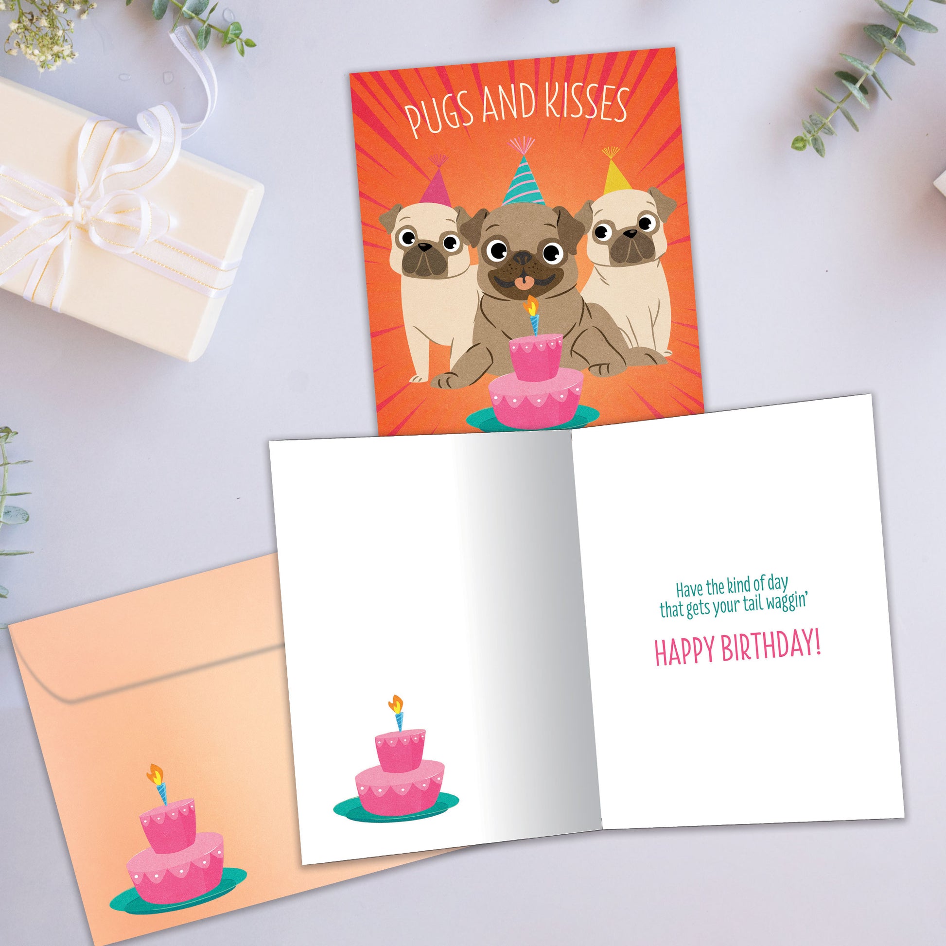 Front and inside view of a Birthday greeting card showcasing a colorful design of 3 pugs and a cake with a birthday message, with a matching envelope.