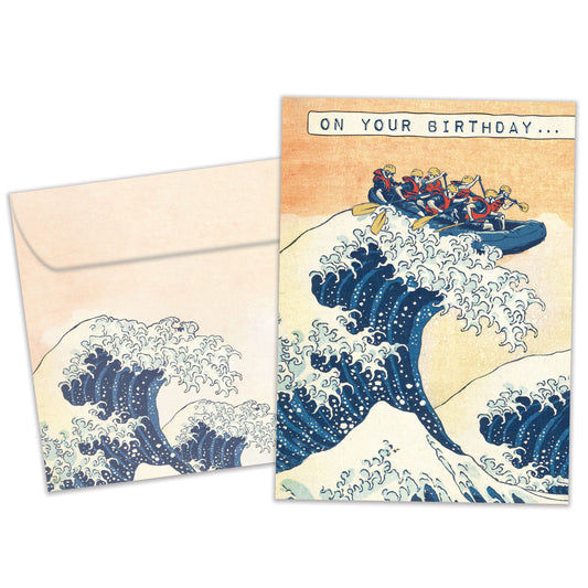 Front view of a Birthday greeting card featuring an illustration of friends in a raft paddling on a giant wave, with a matching envelope.