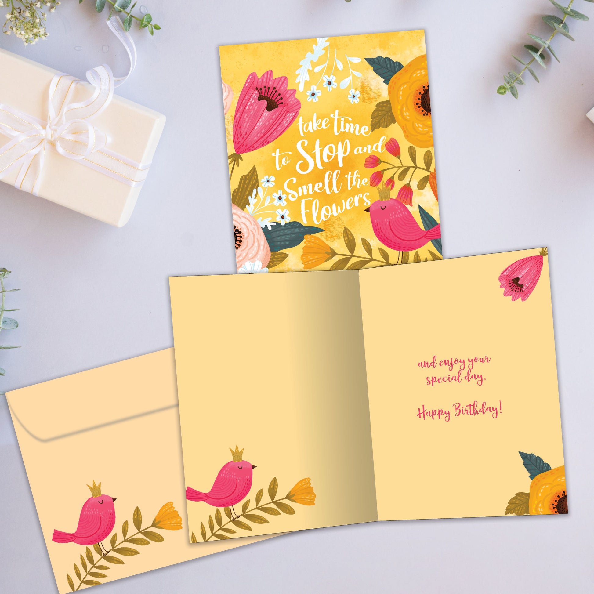 Front and inside view of a Birthday greeting card showcasing a bright floral design with a message about smelling the flowers, with a matching envelope.