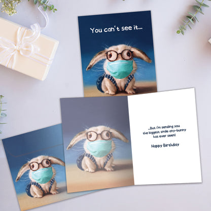 Front and inside view of a Birthday greeting card showcasing a bunny wearing a medical mask with the words "You can't see it...", with a matching envelope.