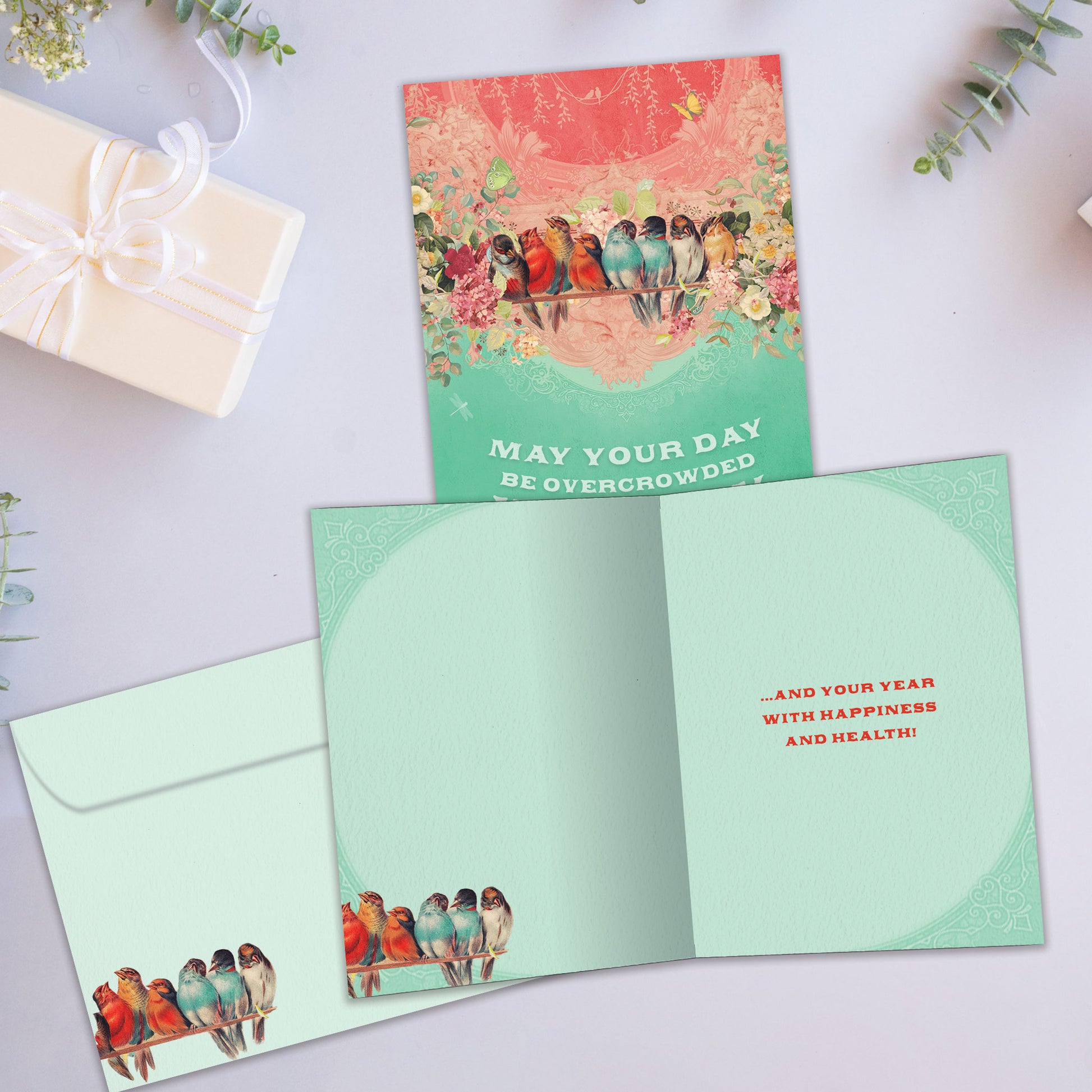 Front and inside view of a Birthday greeting card showcasing birds crowded on a branch with the message "may your day be overcrowded with joy", with a matching envelope.