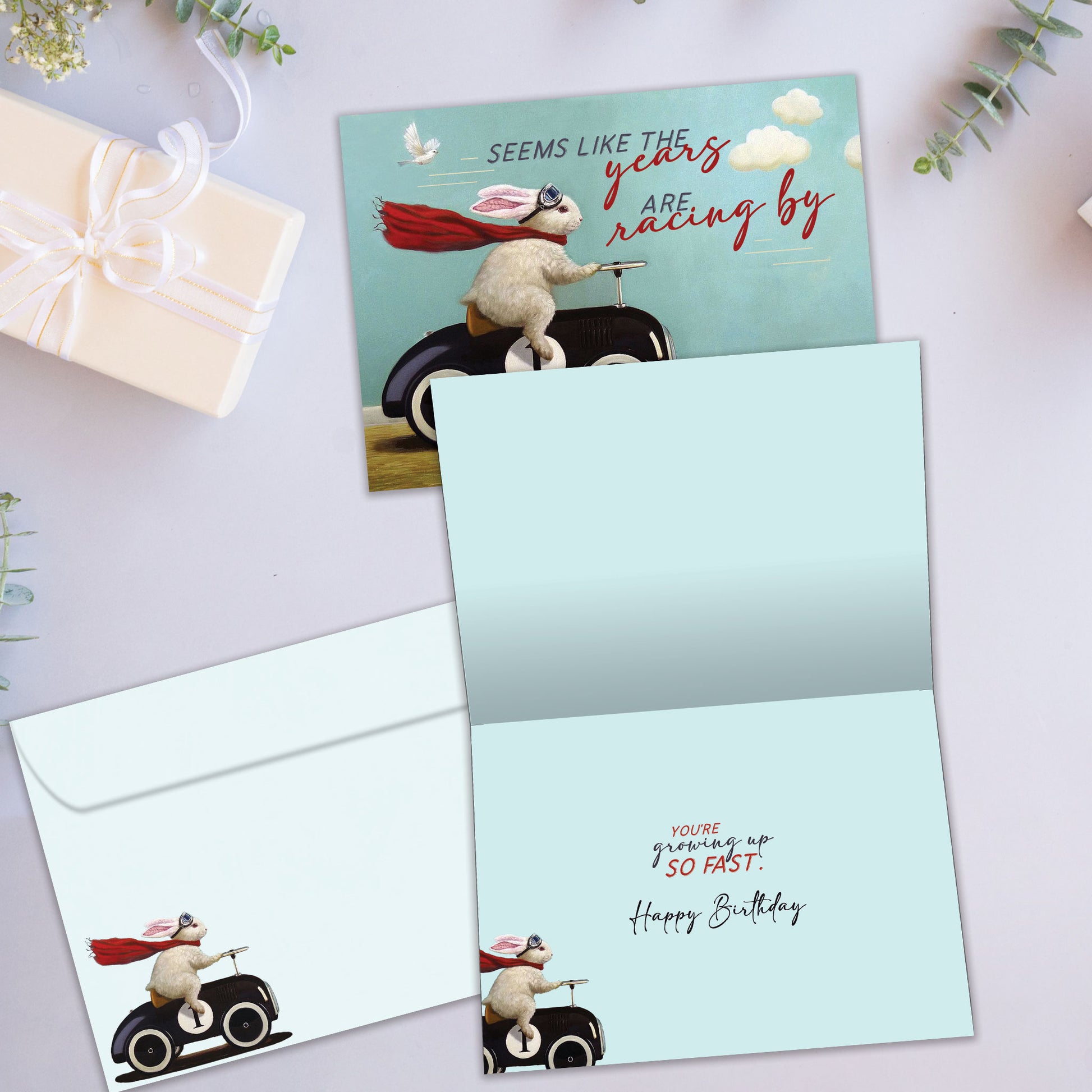 Front and inside view of a Birthday greeting card showcasing a bunny in a car design with the message "the years racing by", with a matching envelope.