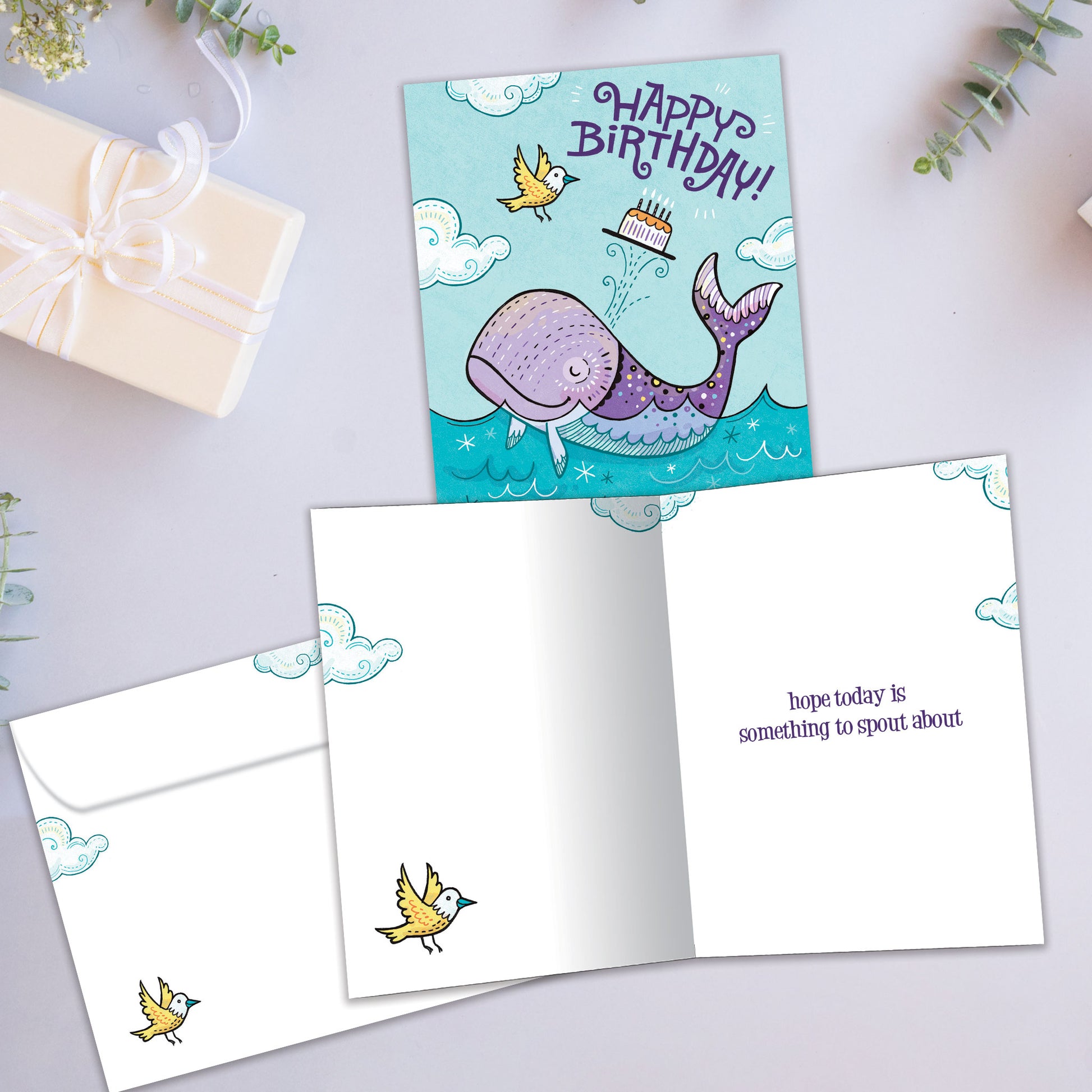 Front and inside view of a Birthday greeting card showcasing a playful illustration of a purple whale with a happy birthday message, with a matching envelope.