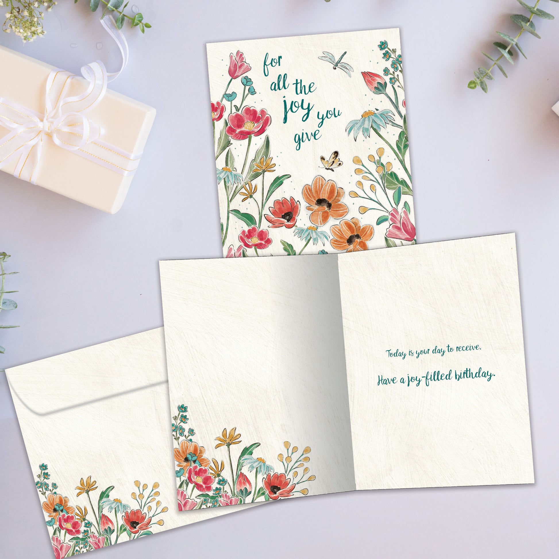 Front and inside view of a Birthday greeting card showcasing the message "for all the joy you give" surrounded by flowers, with a matching envelope.