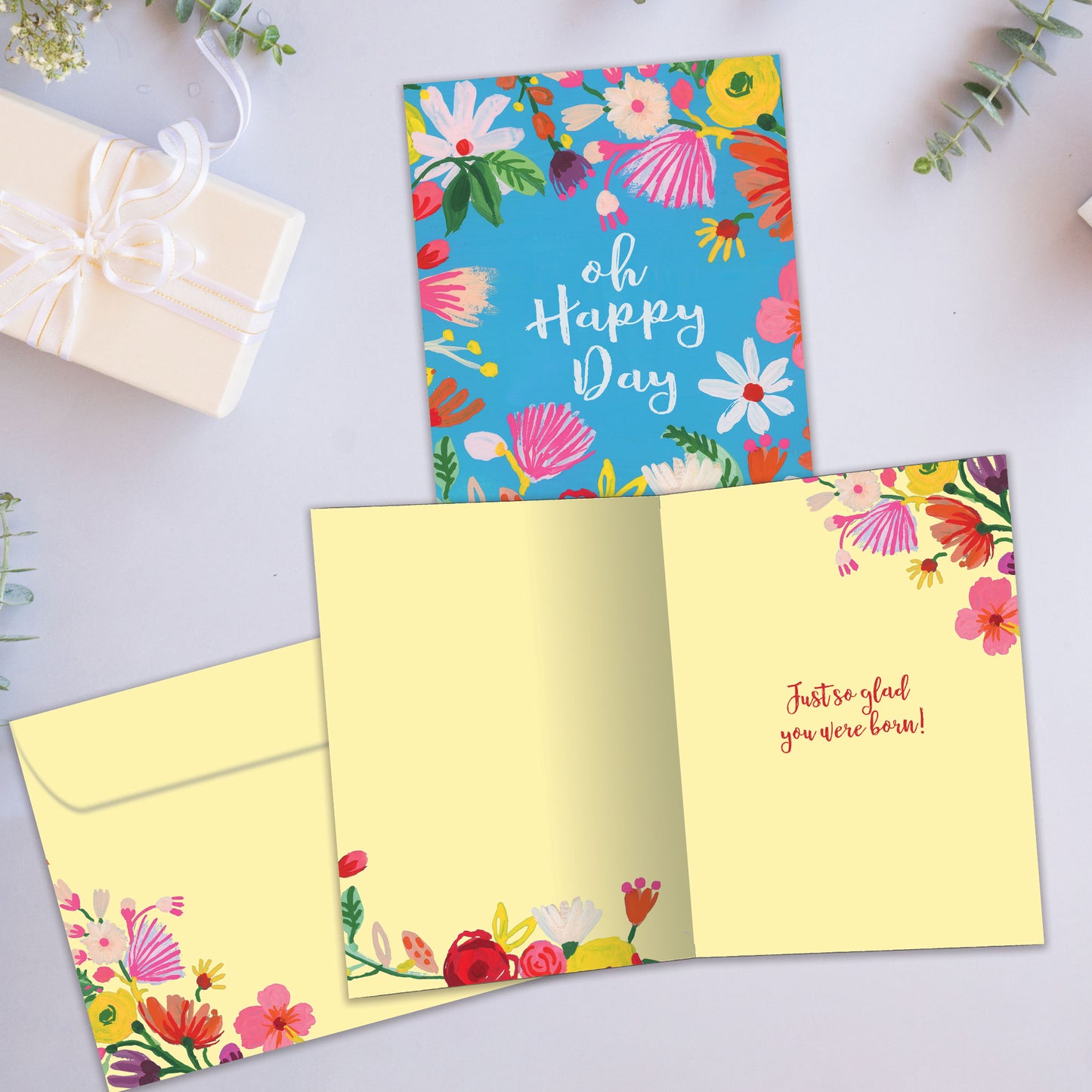 Front and inside view of a Birthday greeting card showcasing the message "oh happy day" surrounded by flowers on a baby blue background, with a matching envelope.