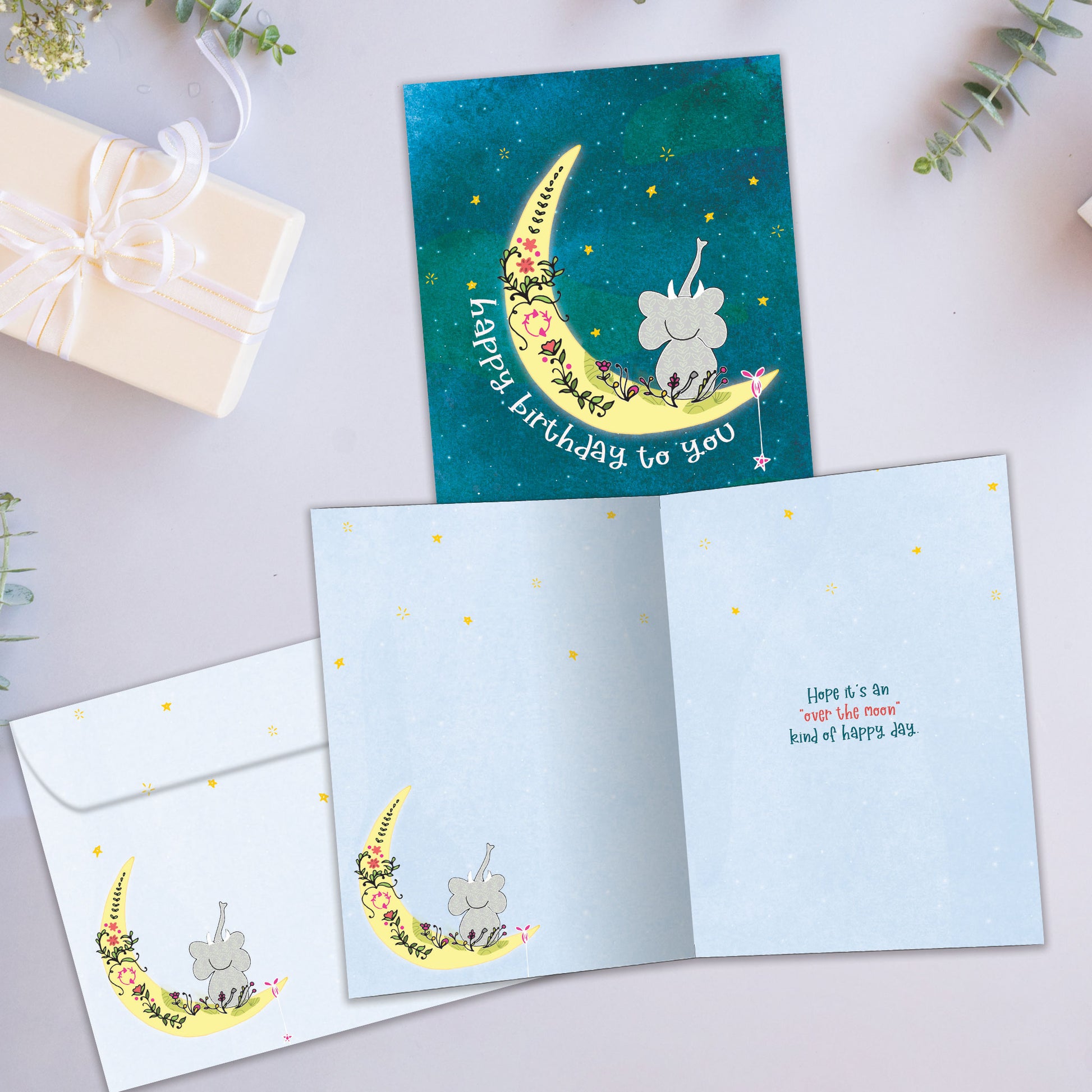 Front and inside view of a Birthday greeting card showcasing an elephant sitting on the moon crescent with a happy birthday message, with a matching envelope.