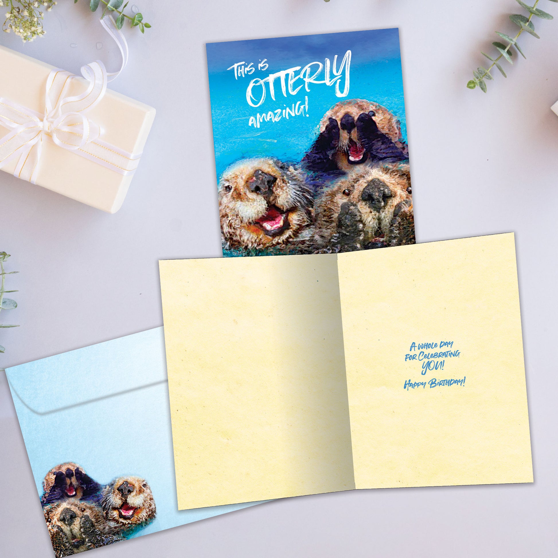 Front and inside view of a Birthday greeting card showcasing otters with the message "this is otterly amazing!", with a matching envelope.