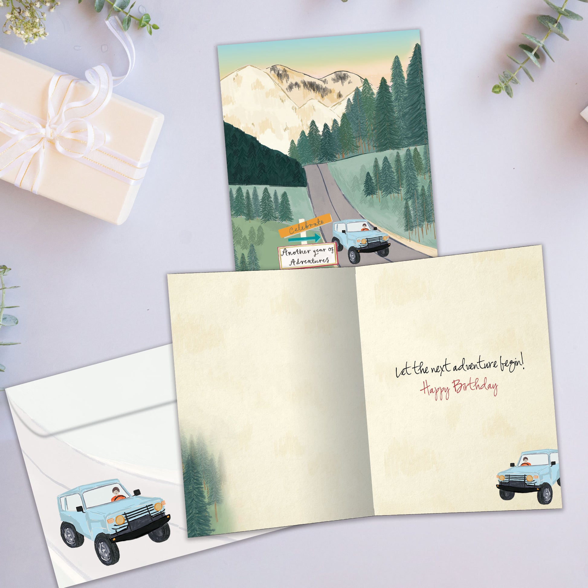 Front and inside view of a Birthday greeting card showcasing an illustration of a car driving on a road through the mountains, with a matching envelope.