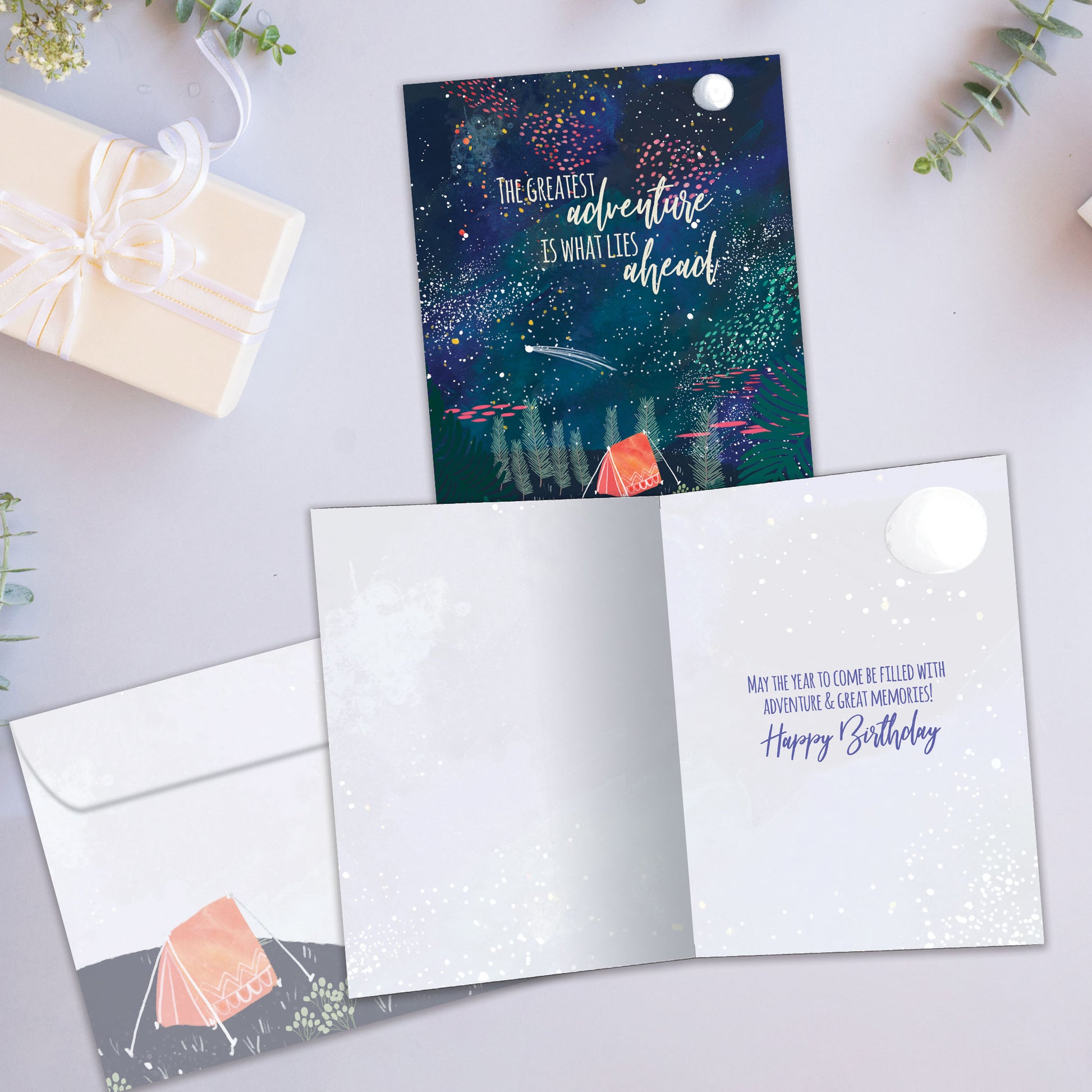 Front and inside view of a Birthday greeting card showcasing a tent in the forest at night with a message about adventures ahead, with a matching envelope.