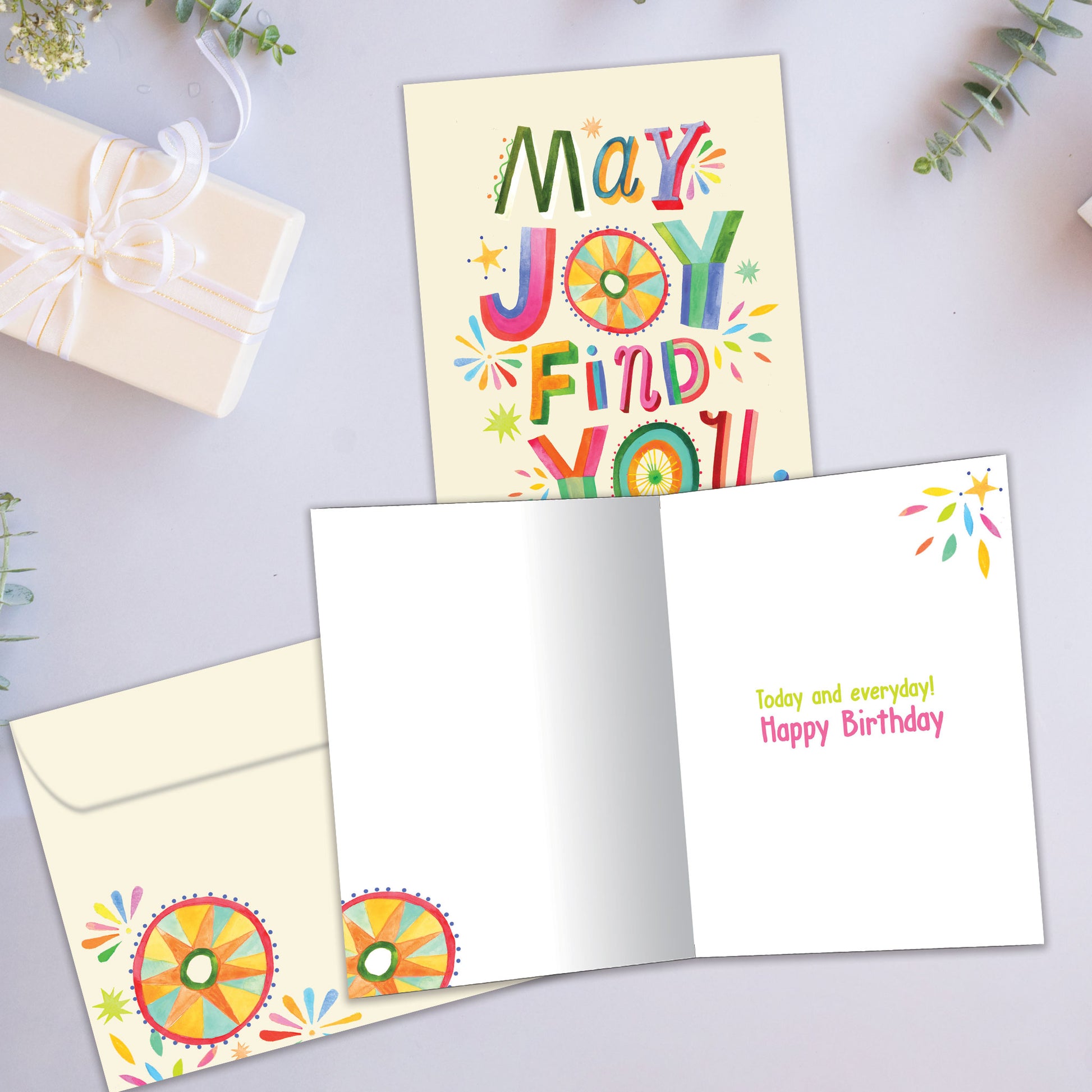Front and inside view of a Birthday greeting card showcasing "may joy find you" in colourful letters on a light yellow background, with a matching envelope.