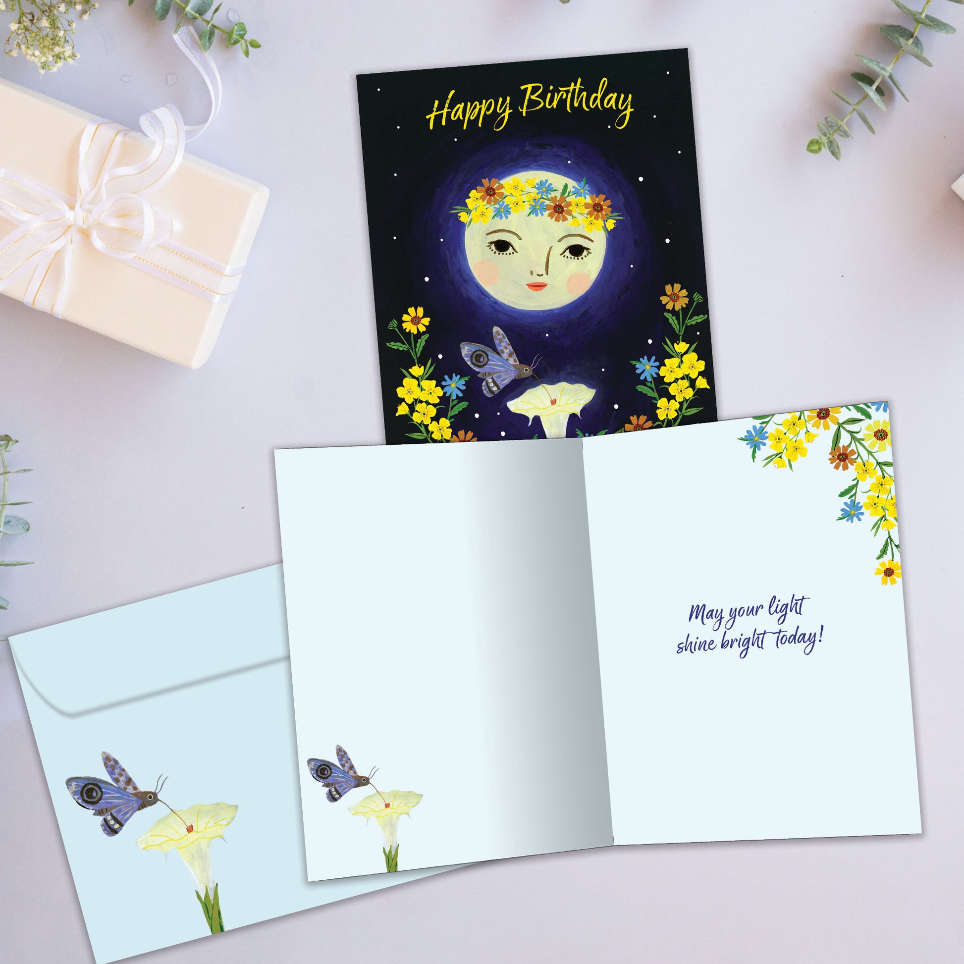 Front and inside view of a Birthday greeting card showcasing a moon, flowers, and the message "Happy Birthday", with a matching envelope.