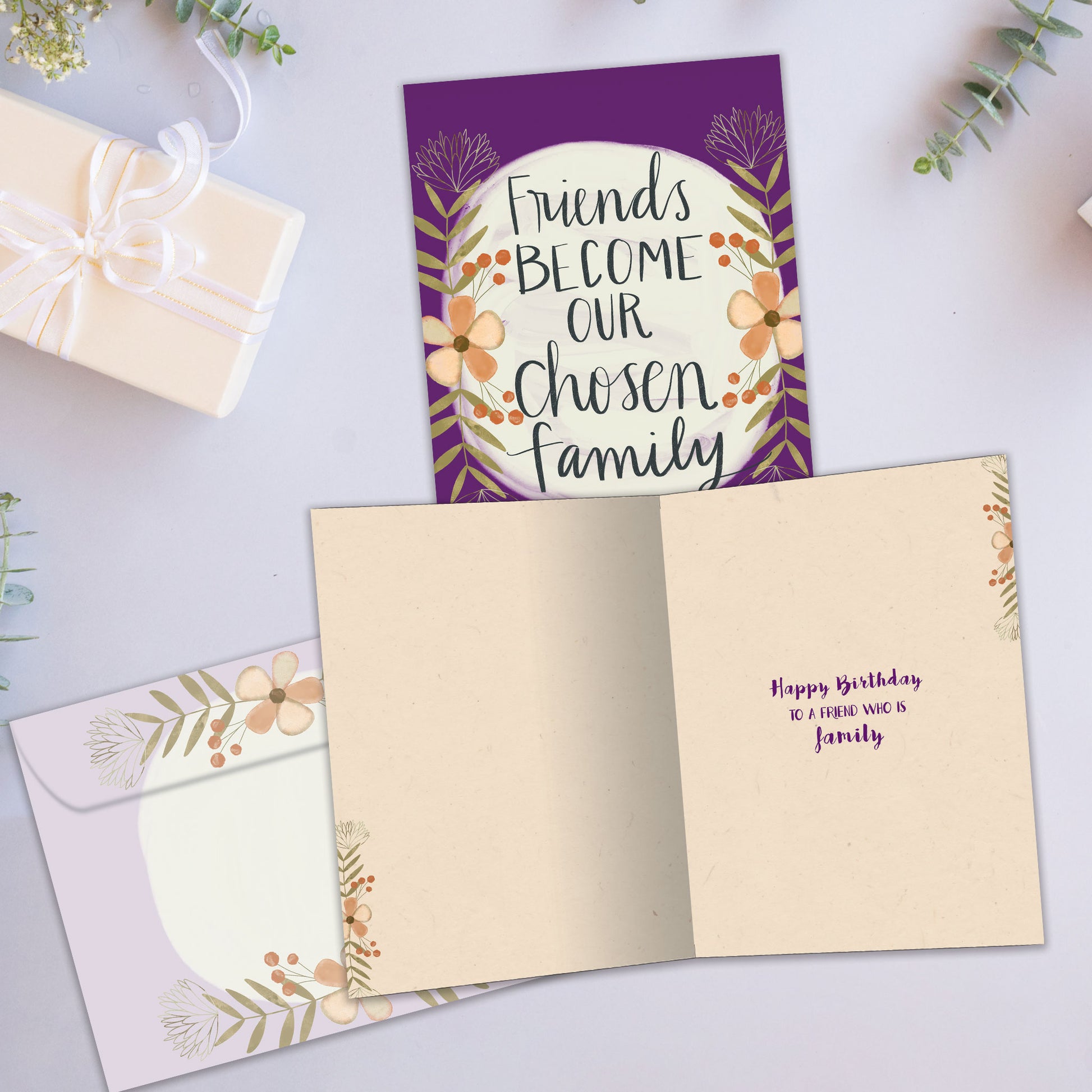 Front and inside view of a birthday greeting card showcasing the message "friends become our chosen family" surrounded by flowers on a purple background, with a matching envelope.