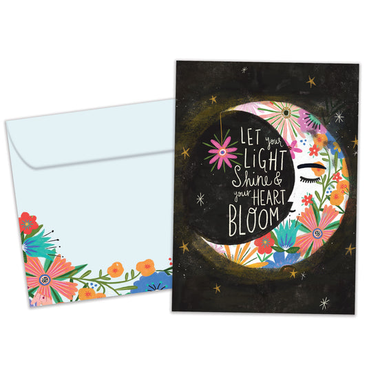 Front view of a birthday greeting card featuring an illustration of a floral crescent moon with a message about letting your light shine, with a matching envelope.