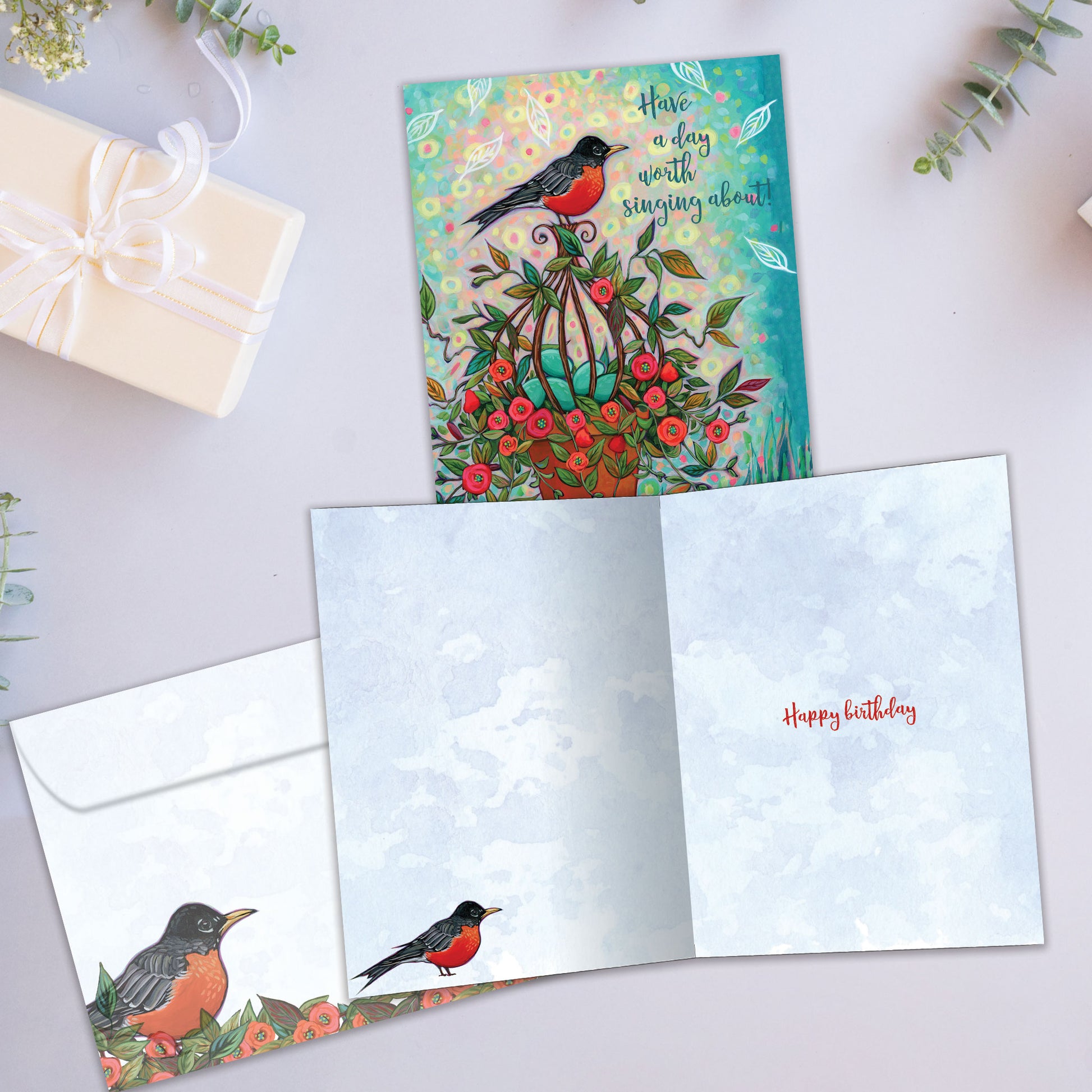 Front and inside view of a birthday greeting card showcasing a colourful illustration of a robin with the message "have a day worth singing about", with a matching envelope.