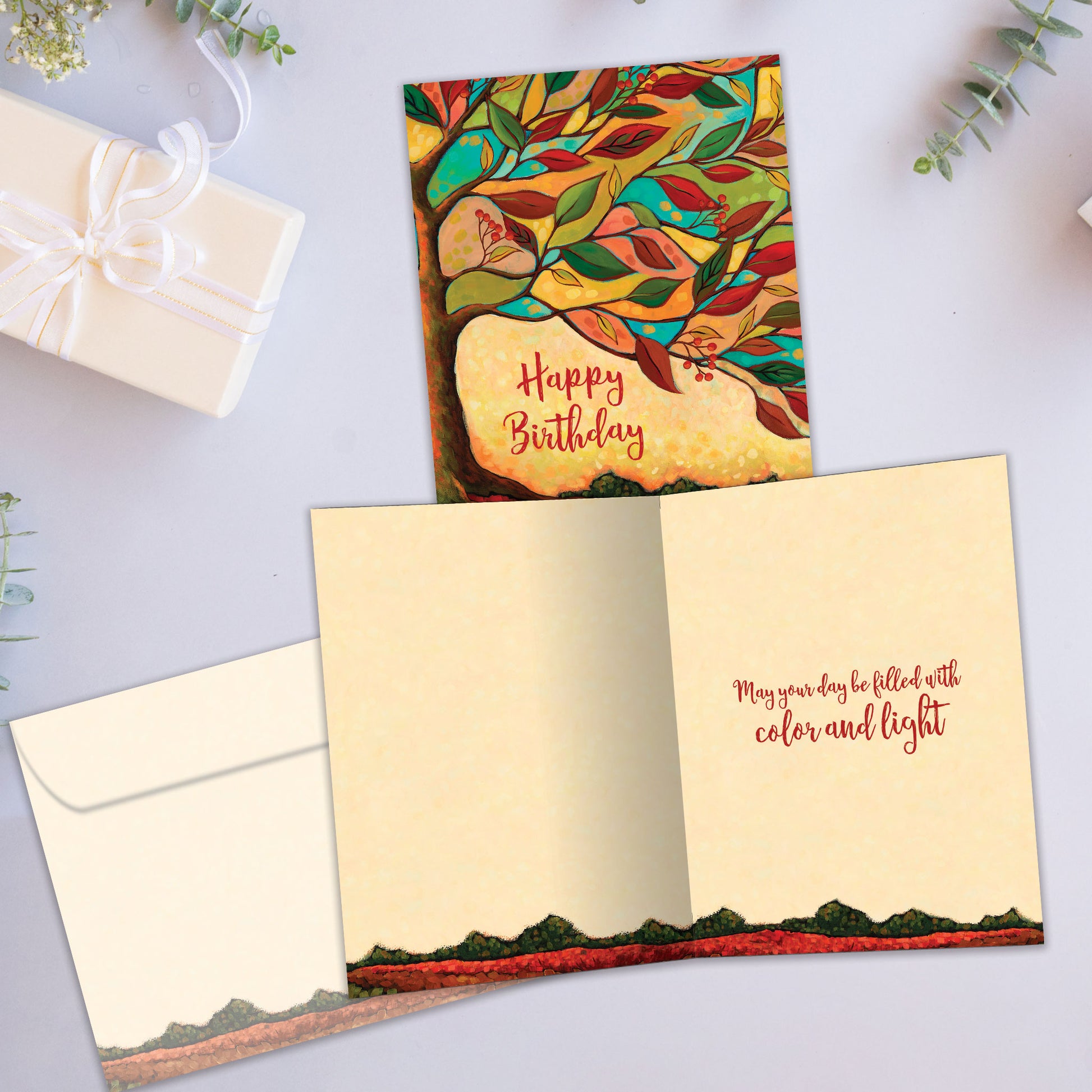 Front and inside view of a birthday greeting card showcasing the message "happy birthday" surrounded by a tree and vibrant fall colours, with a matching envelope.