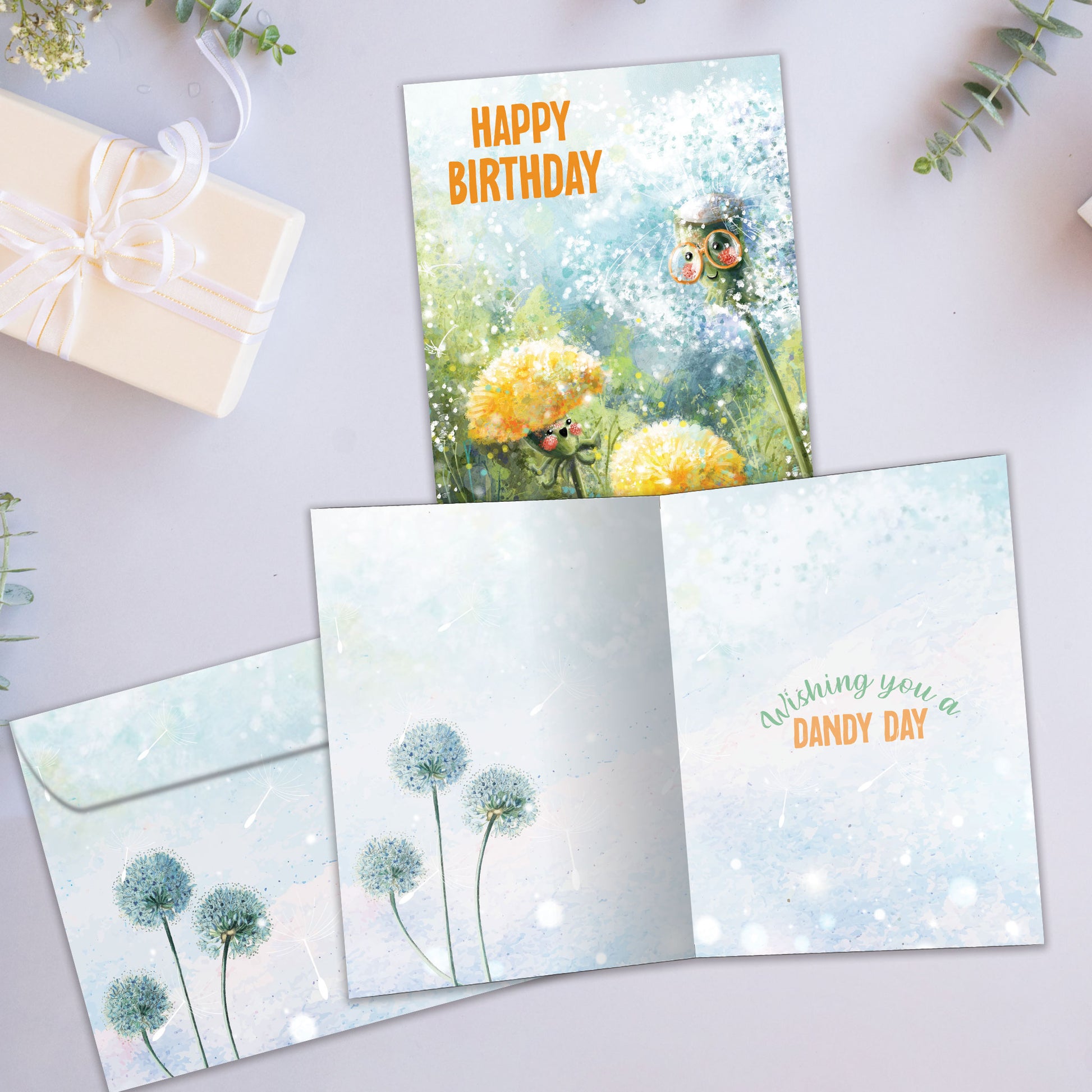 Front and inside view of a birthday greeting card showcasing an illustration of dandelions in soft colours with the message "happy birthday", with a matching envelope.