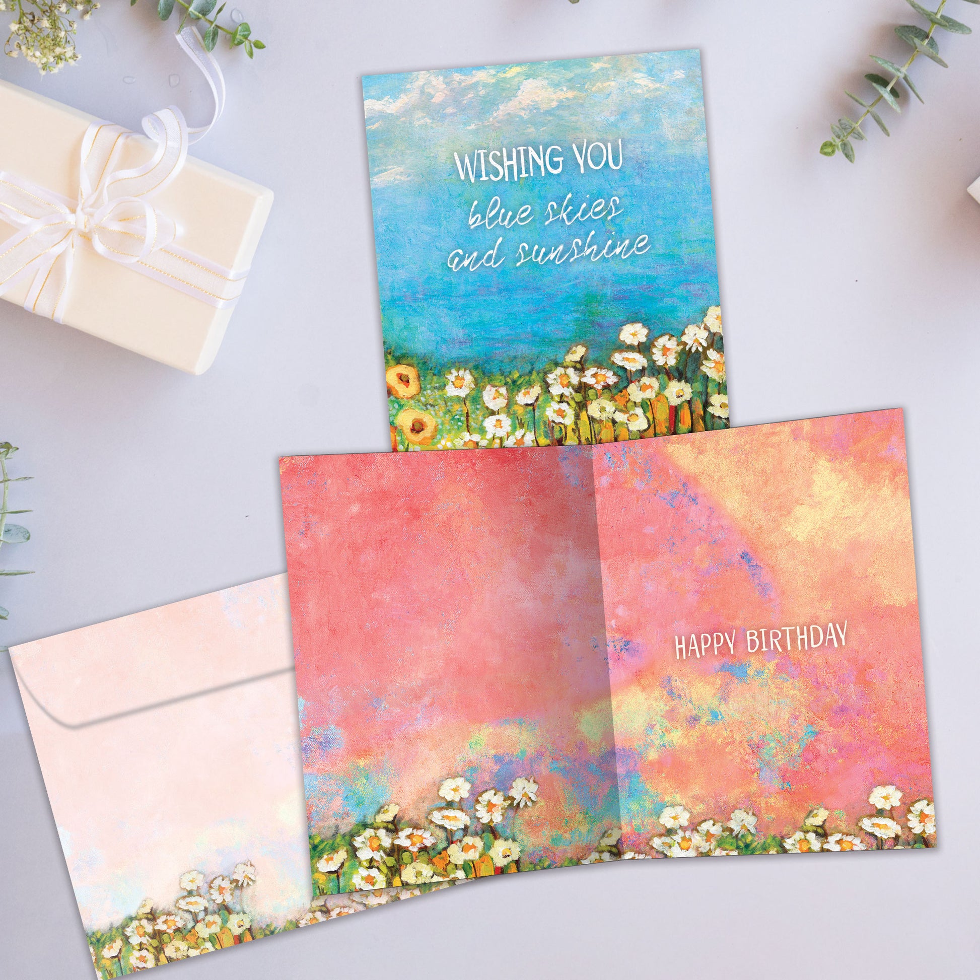 Front and inside view of a birthday greeting card showcasing the message "wishing you blue skies and sunshine" with an illustration of blue skies and flowers, with a matching envelope.