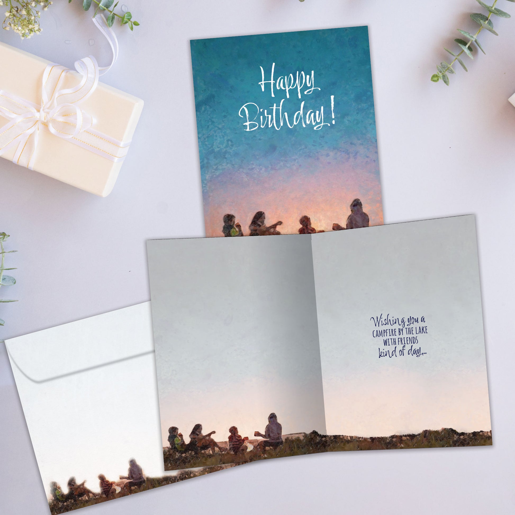 Front and inside view of a birthday greeting card showcasing an illustration of a family sitting and playing guitar around a campfire with the message "Happy Birthday!", with a matching envelope.