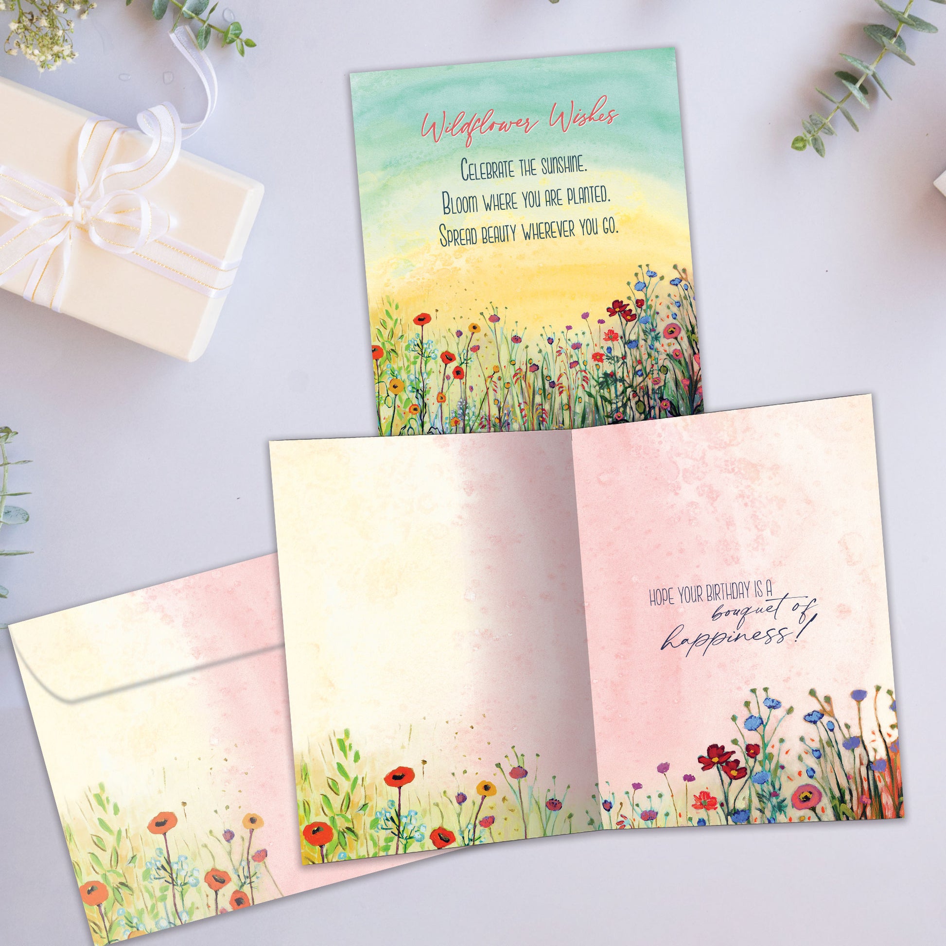 Front and inside view of a birthday greeting card showcasing a beautiful illustration of a flowery field on a soft pastel background, with a matching envelope.