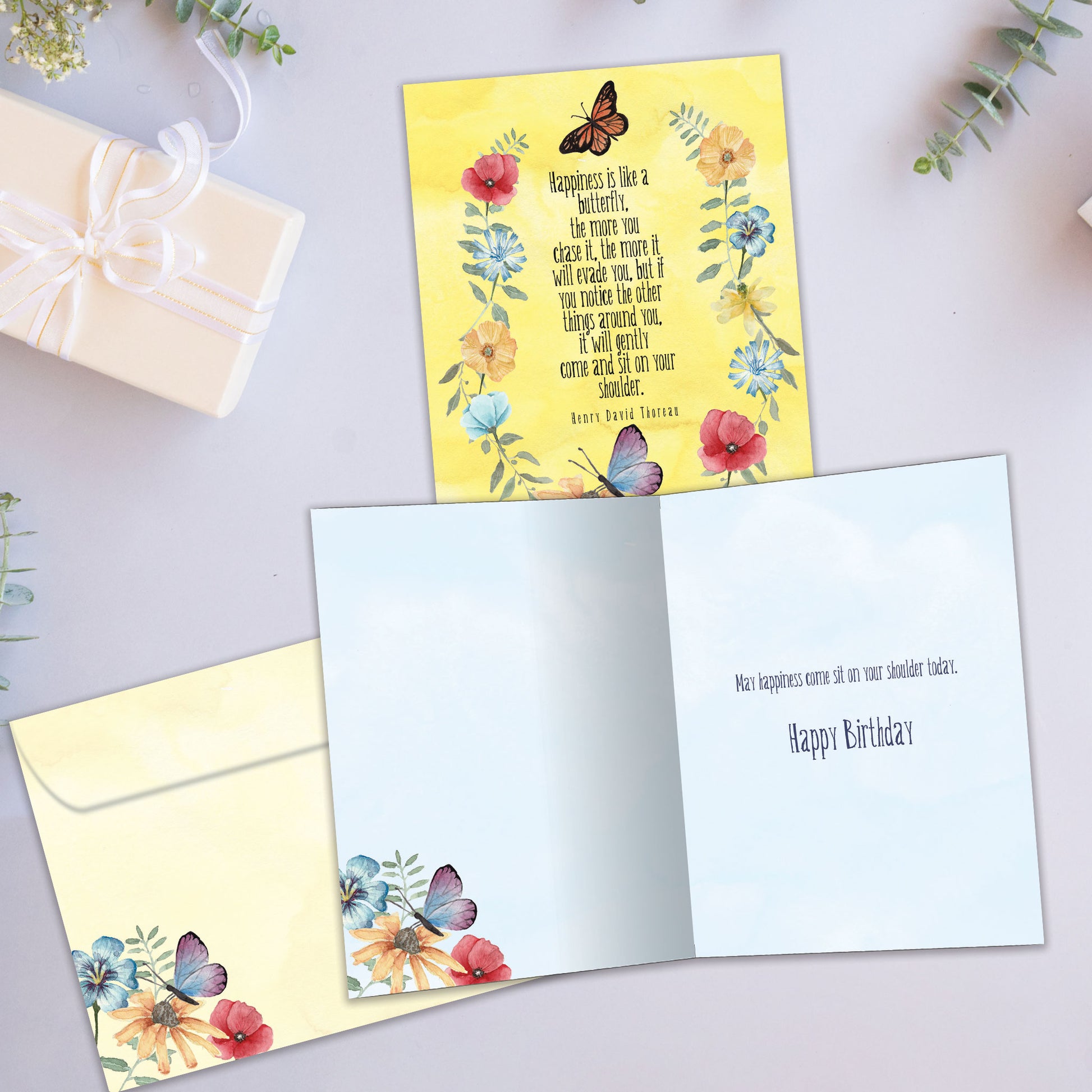 Front and inside view of a birthday greeting card showcasing a saying from Henry David Thoreau about happiness, surrounded by flowers and butterflies, with a matching envelope.