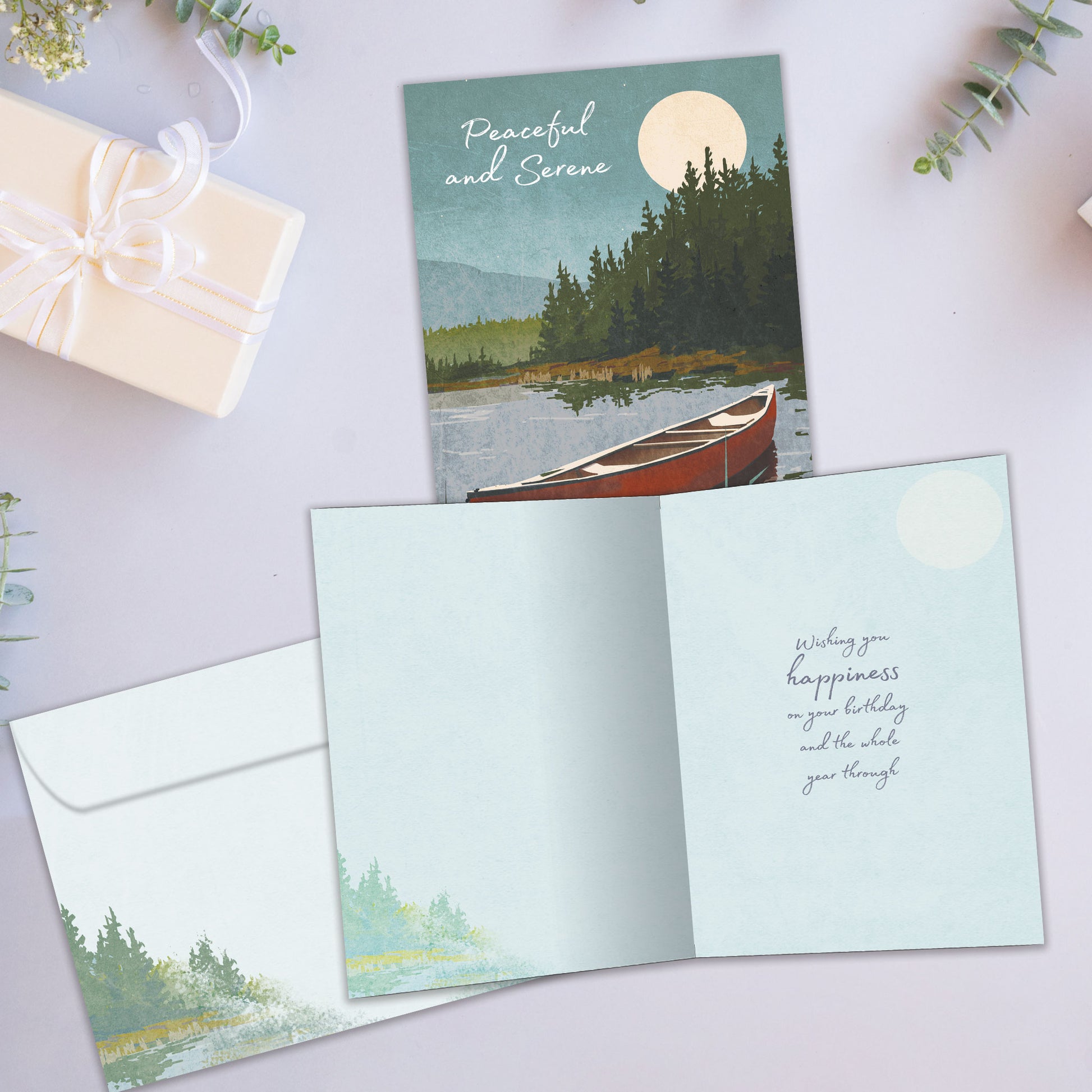 Front and inside view of a birthday greeting card showcasing an illustration of a canoe on a lake with the message "Peaceful and Serene", with a matching envelope.