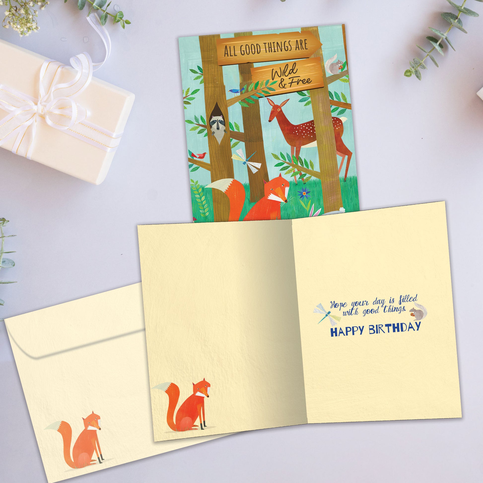 Front and inside view of a birthday greeting card showcasing an illustration of a forest scene with animals and a message about being wild and free, with a matching envelope.