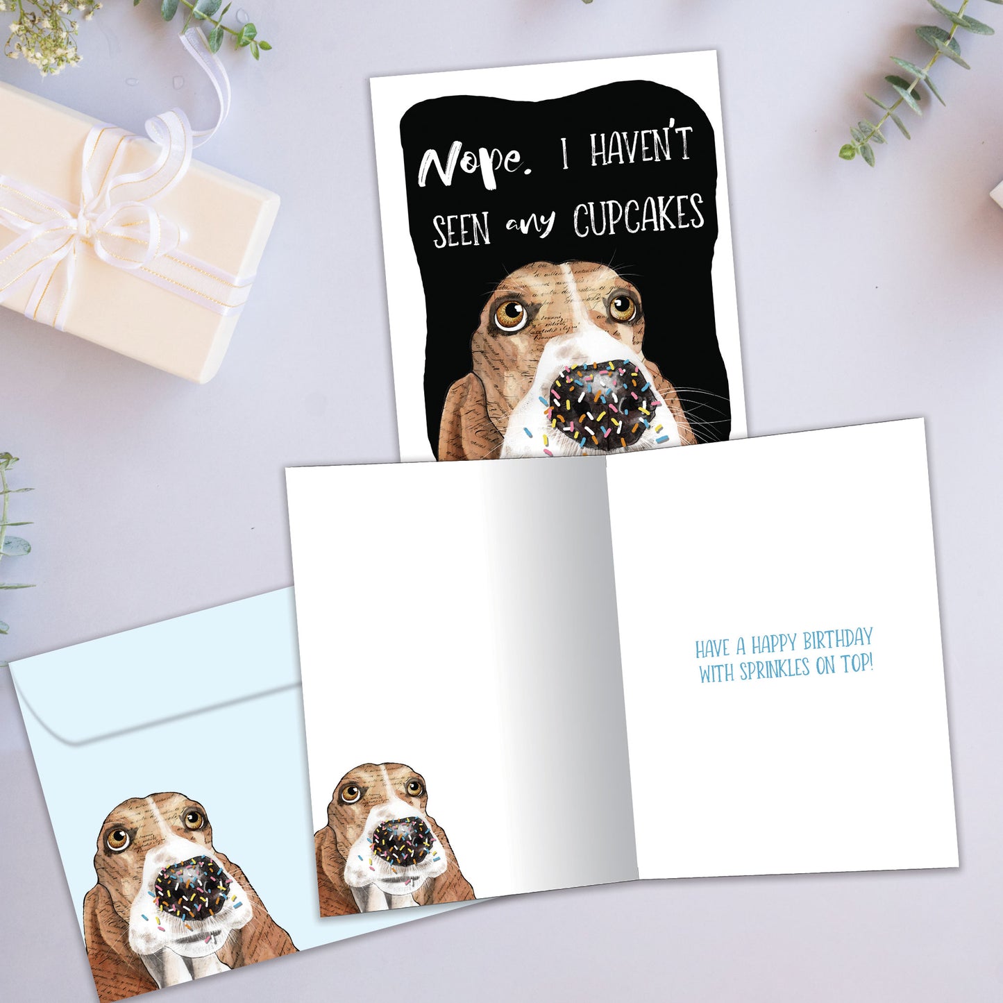 Front and inside view of a birthday greeting card showcasing an illustration of a dog’s face denying eating the cupcakes, with a matching envelope.