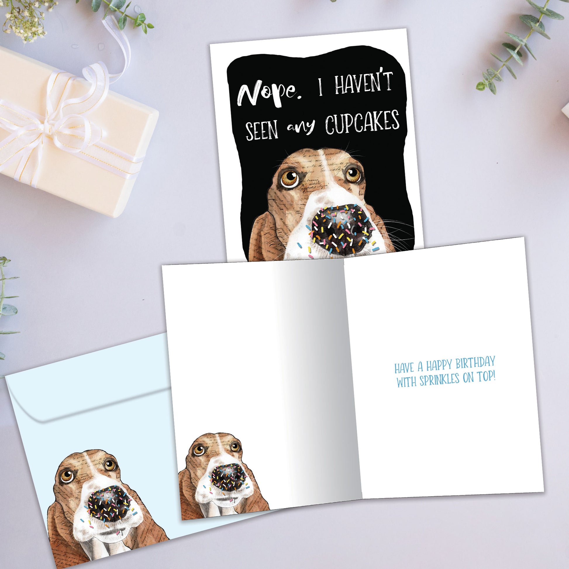 Front and inside view of a birthday greeting card showcasing an illustration of a dog’s face denying eating the cupcakes, with a matching envelope.