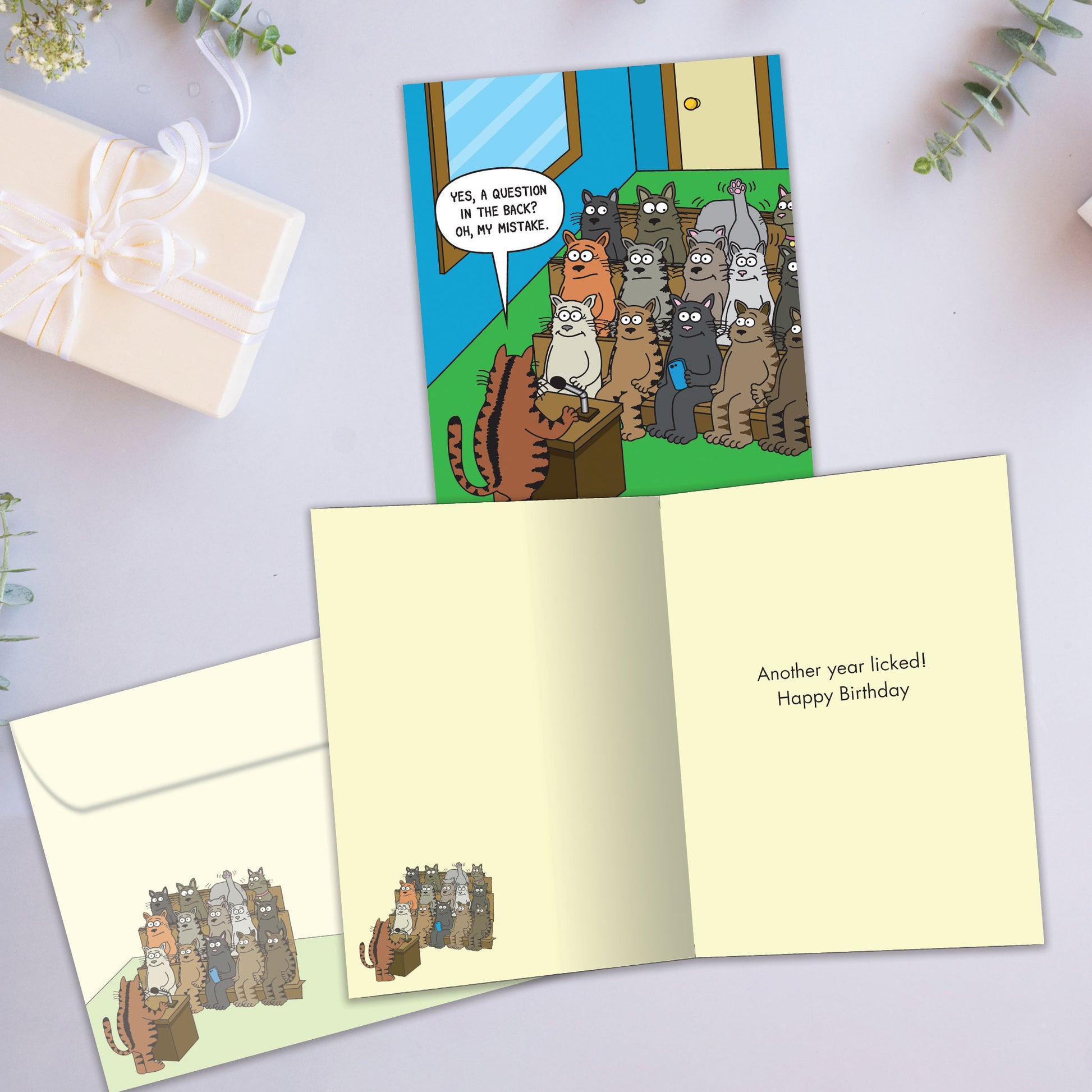 Front and inside view of a birthday greeting card showcasing a humorous comic of cats in a classroom setting, with a matching envelope.