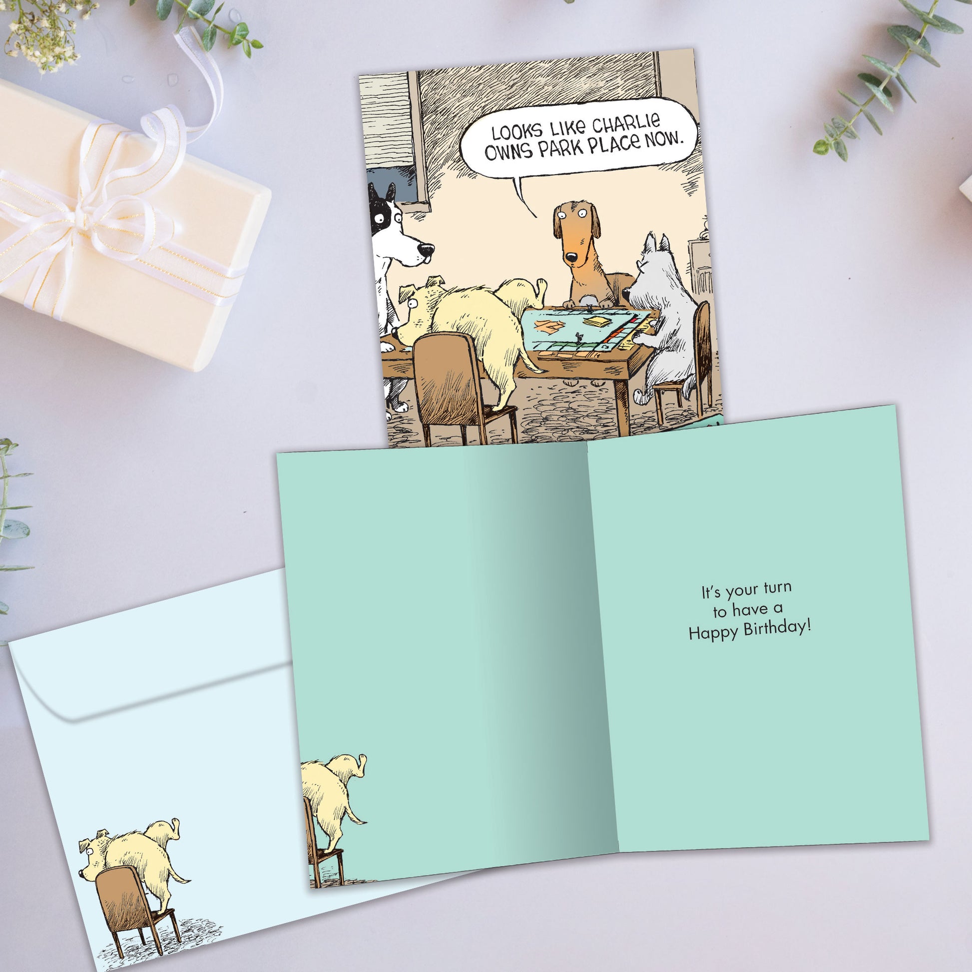 Front and inside view of a birthday greeting card showcasing a funny comic of dogs playing Monopoly, with a matching envelope.