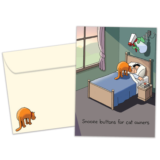 Front view of a Birthday greeting card featuring a cat waking up its owner and the message “Snooze buttons for cat owners”, with a matching envelope. 
