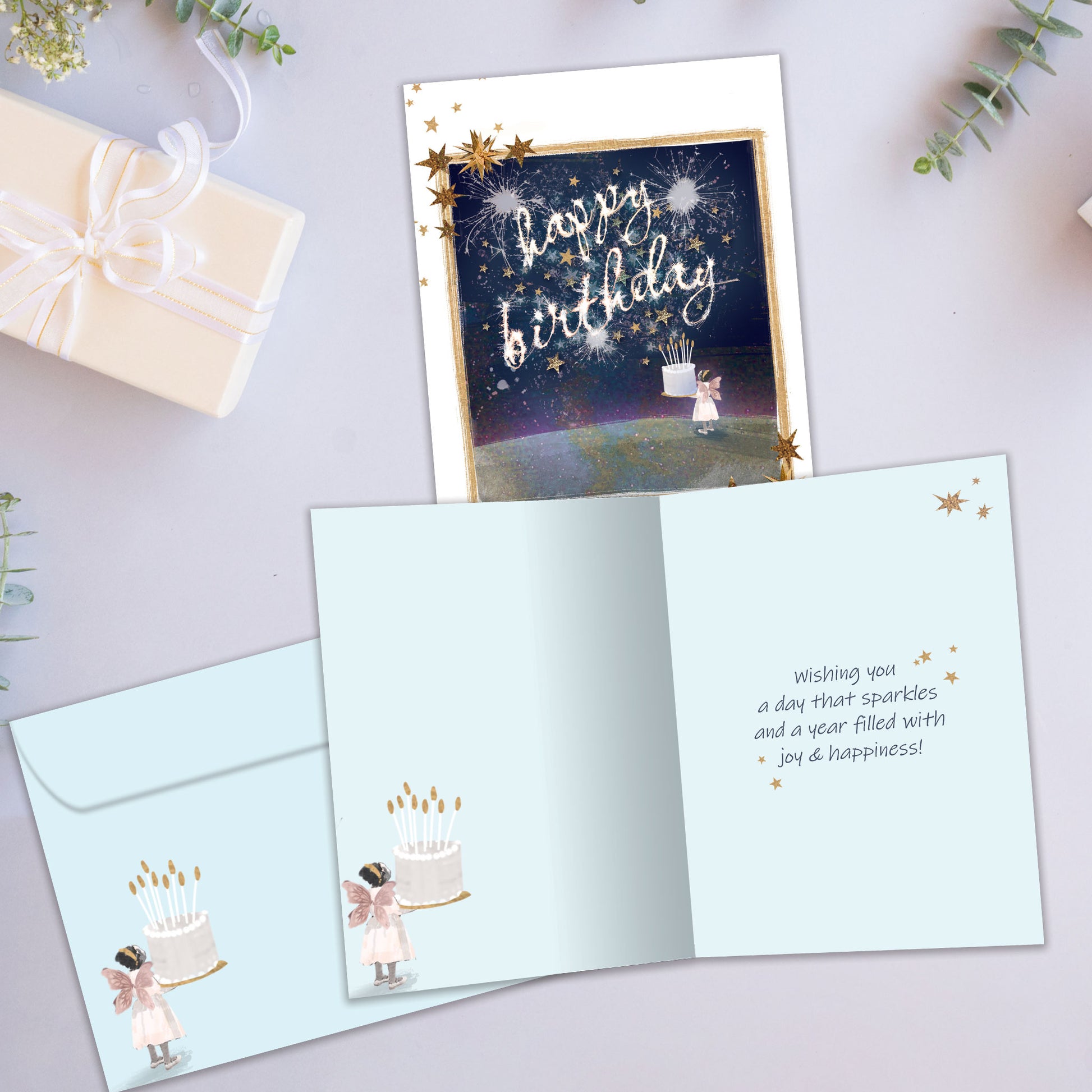 Front and inside view of a Birthday greeting card showcasing a fairy holding a birthday cake and the message "Happy Birthday", with a matching envelope. 