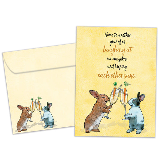 Front view of a Birthday greeting card featuring two rabbits with champagne glasses and a message about “us”, with a matching envelope. 