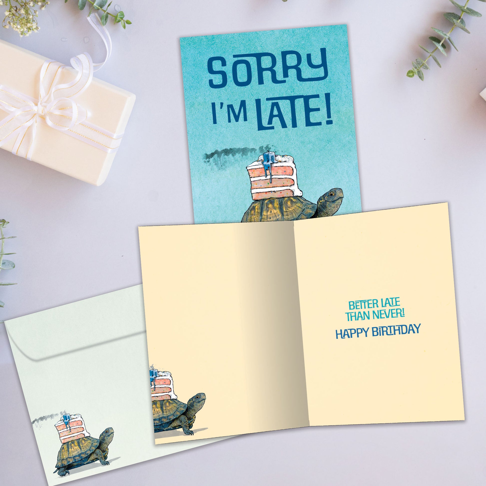 Front and inside view of a Birthday greeting card showcasing a turtle with a cake on it’s back and the message "Sorry I’m late", with a matching envelope. 