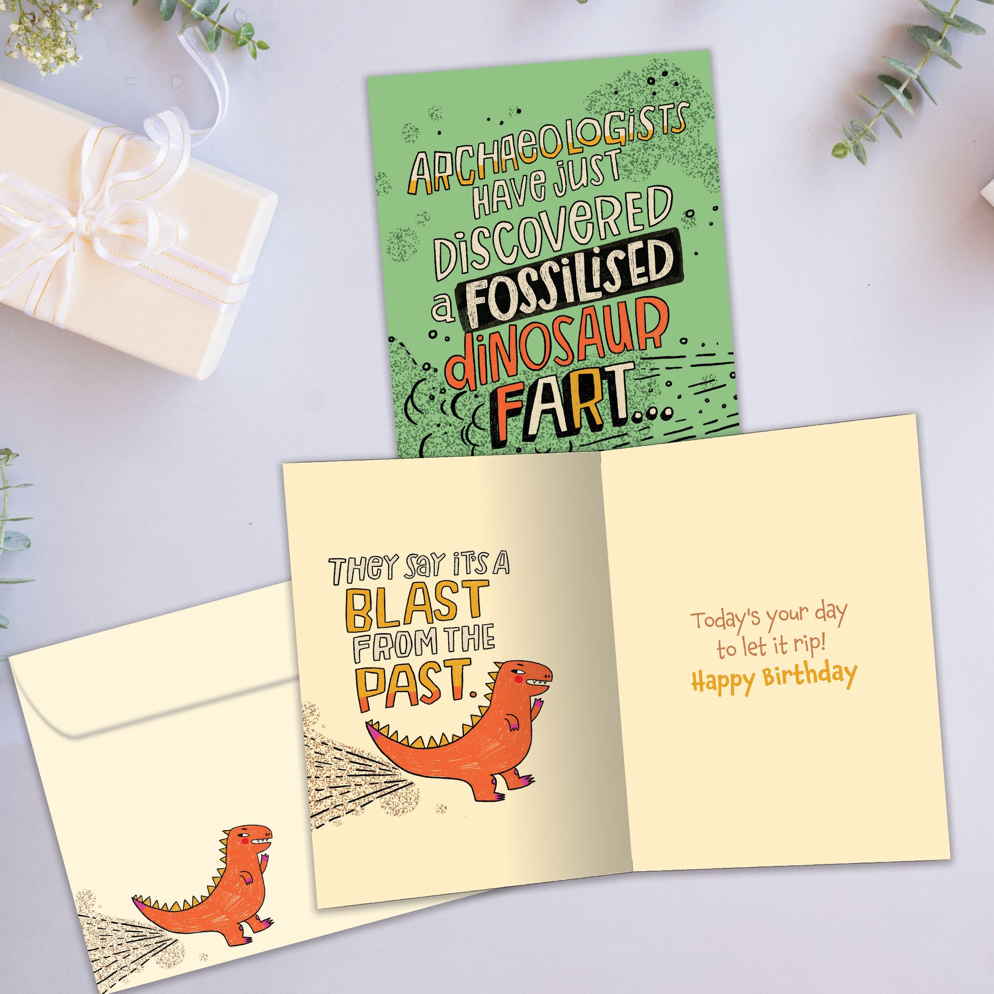 Front and inside view of a Birthday greeting card with a green background and a funny message about a fossilised dinosaur fart, with a matching envelope