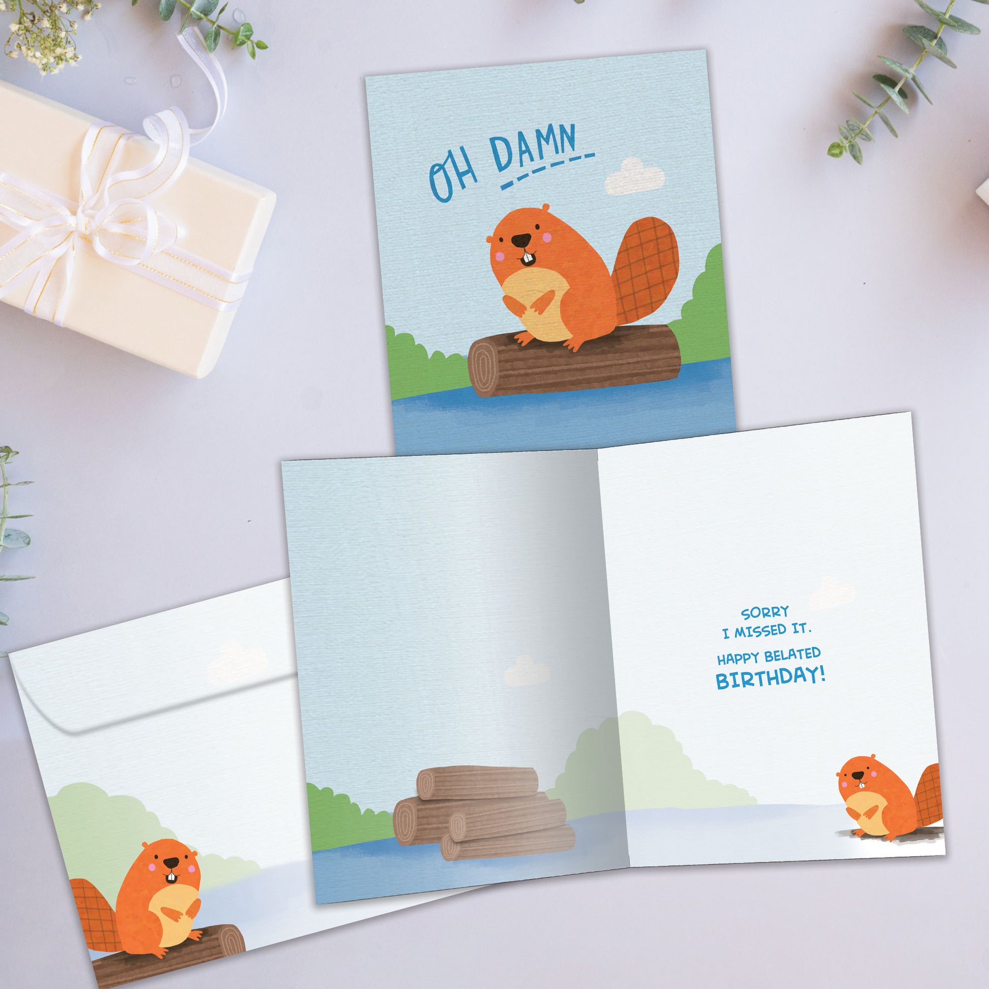 Front and inside view of a Birthday greeting card showcasing a beaver floating on a log with the message "oh damn", with a matching envelope.