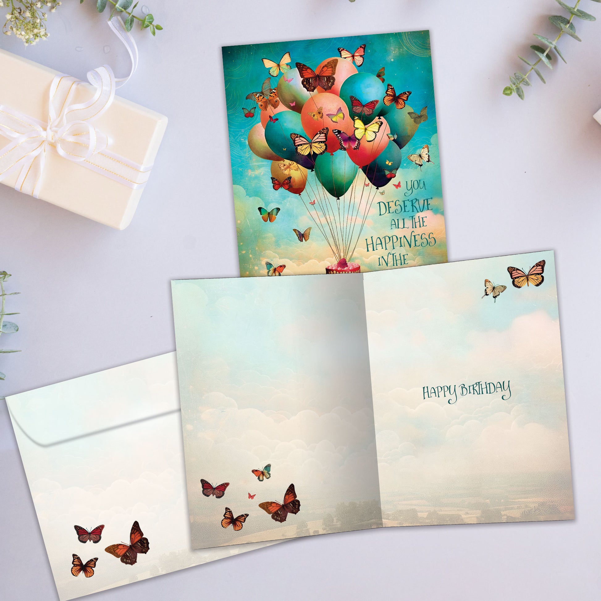 Front and inside view of a Birthday greeting card featuring balloons floating a cake in the sky and butterflies, with a matching envelope