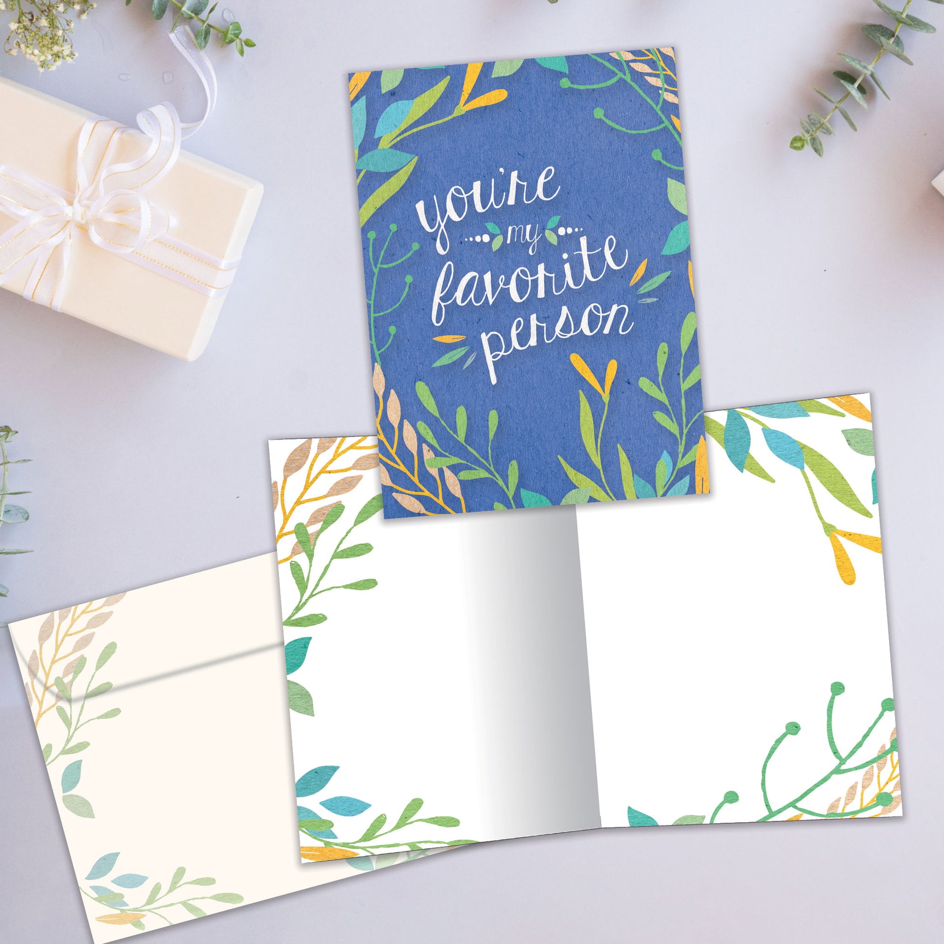 Front and inside view of an All Occasion greeting card showcasing the message 'You're my favorite person' surrounded by soft-coloured foliage on a blue background, with a matching envelope.
