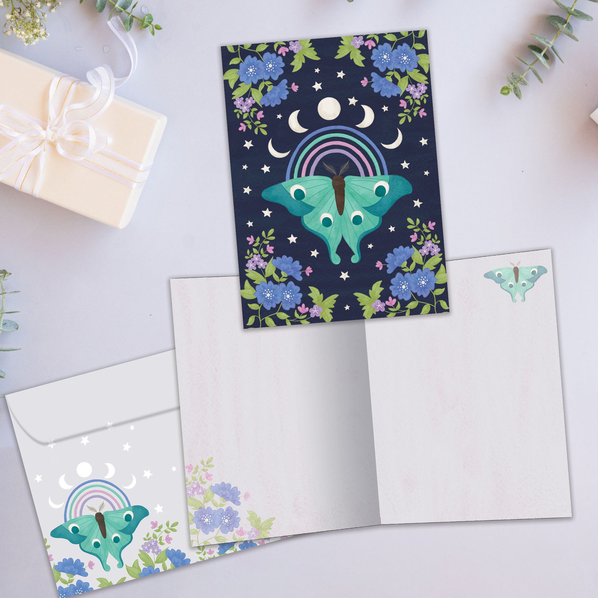 Front and inside view of an All Occasion greeting card showcasing a detailed moth illustration with moon phases and flowers on a dark blue background, with a matching envelope.