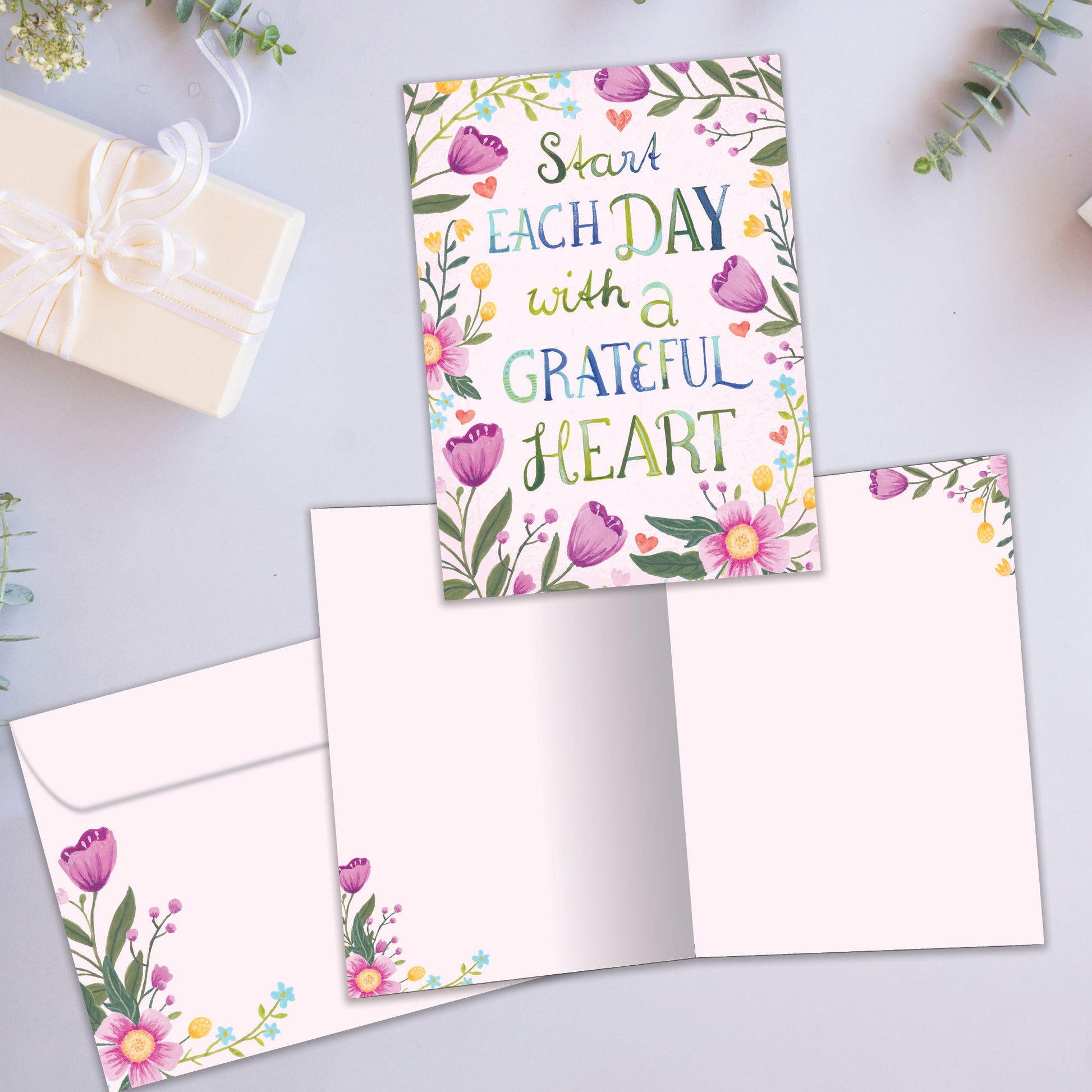 Front and inside view of an All Occasion greeting card featuring the message 'Start each day with a grateful heart' surrounded by delicate flowers, plus a matching envelope.