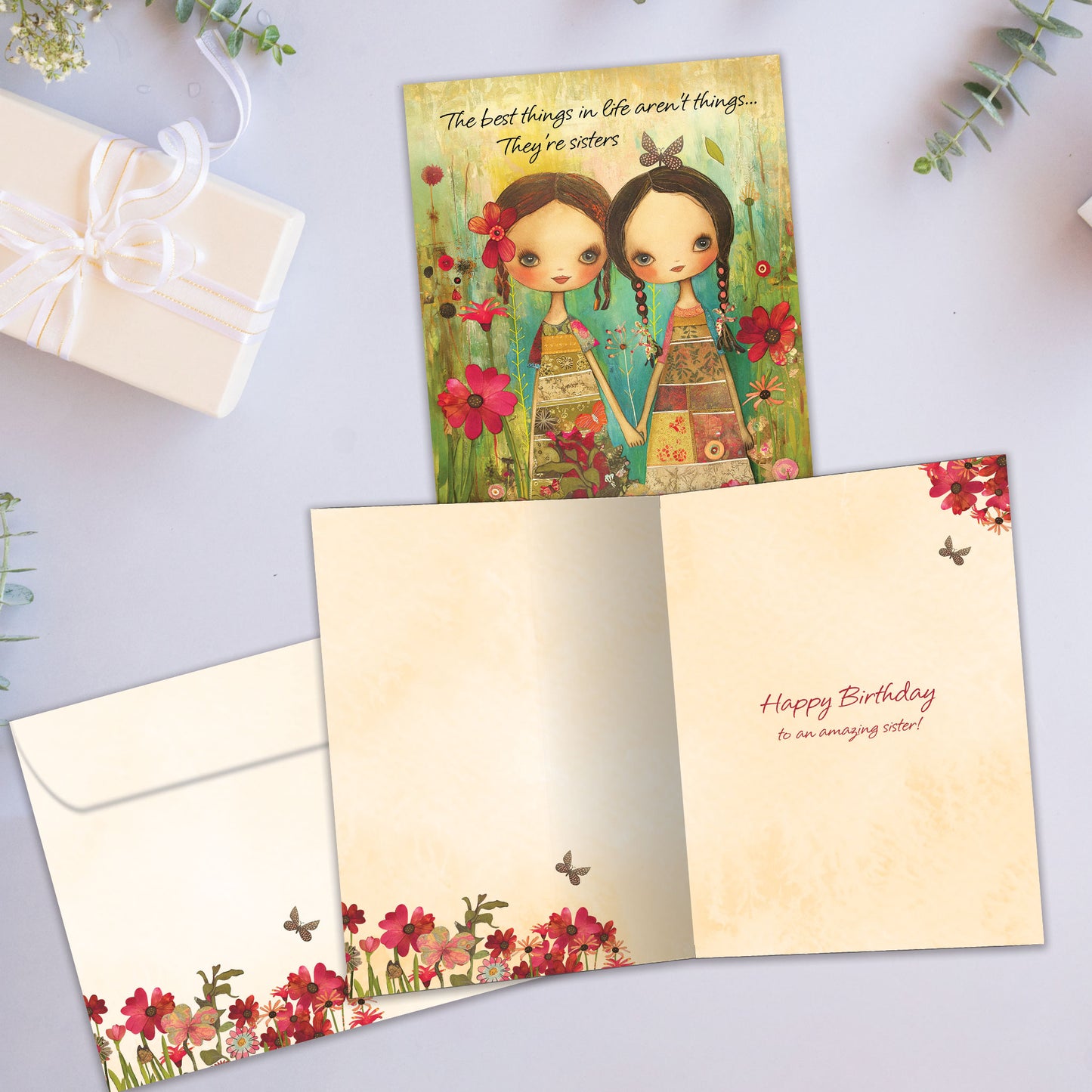 Front and inside view of a Birthday greeting card showcasing an illustration of two sisters holding hands surrounded by colorful flowers, with a matching envelope.