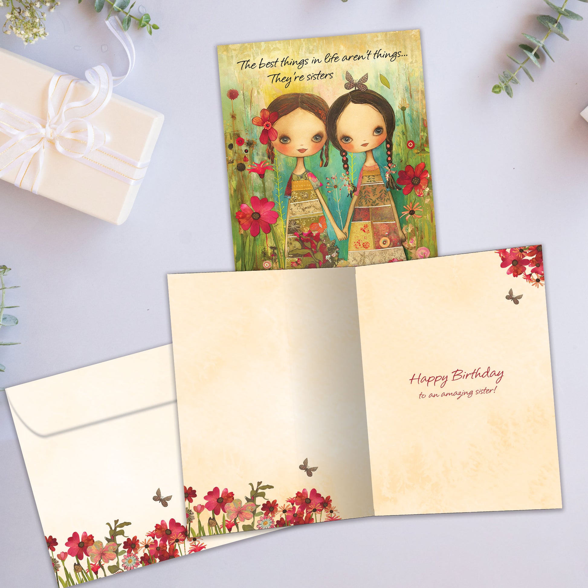 Front and inside view of a Birthday greeting card showcasing an illustration of two sisters holding hands surrounded by colorful flowers, with a matching envelope.