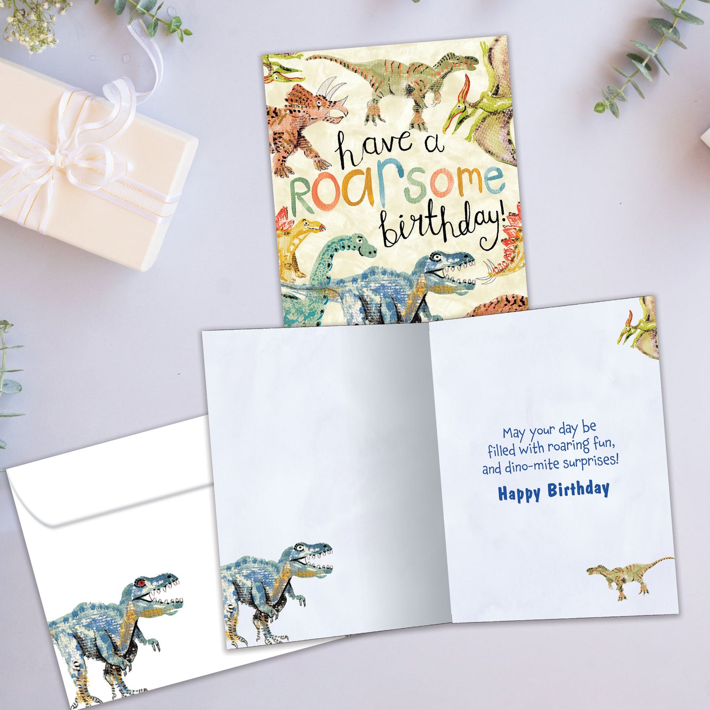 Front and inside view of a Birthday greeting card showcasing an illustration of dinosaurs surrounding a fun birthday message, with a matching envelope.