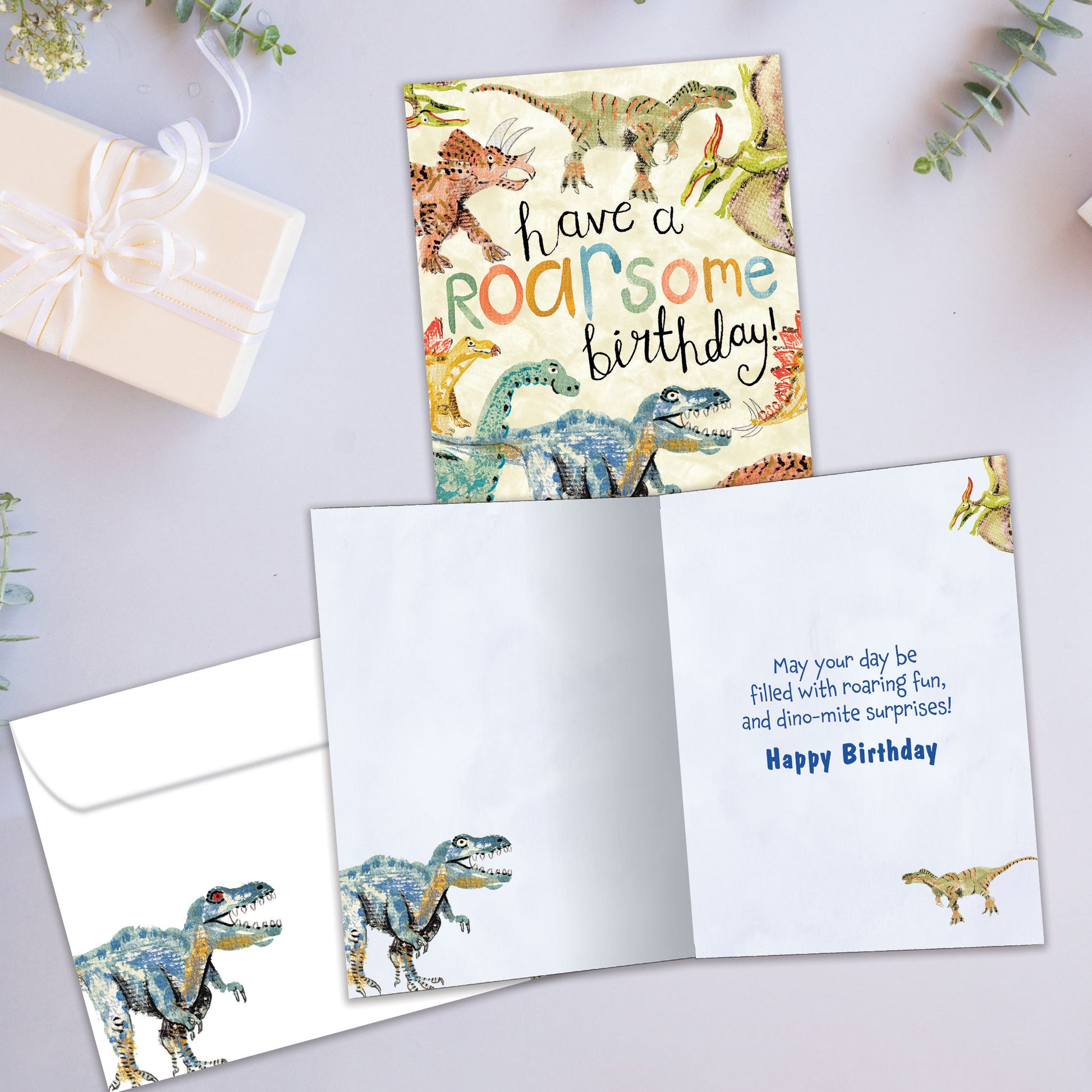 Front and inside view of a Birthday greeting card showcasing an illustration of dinosaurs surrounding a fun birthday message, with a matching envelope.