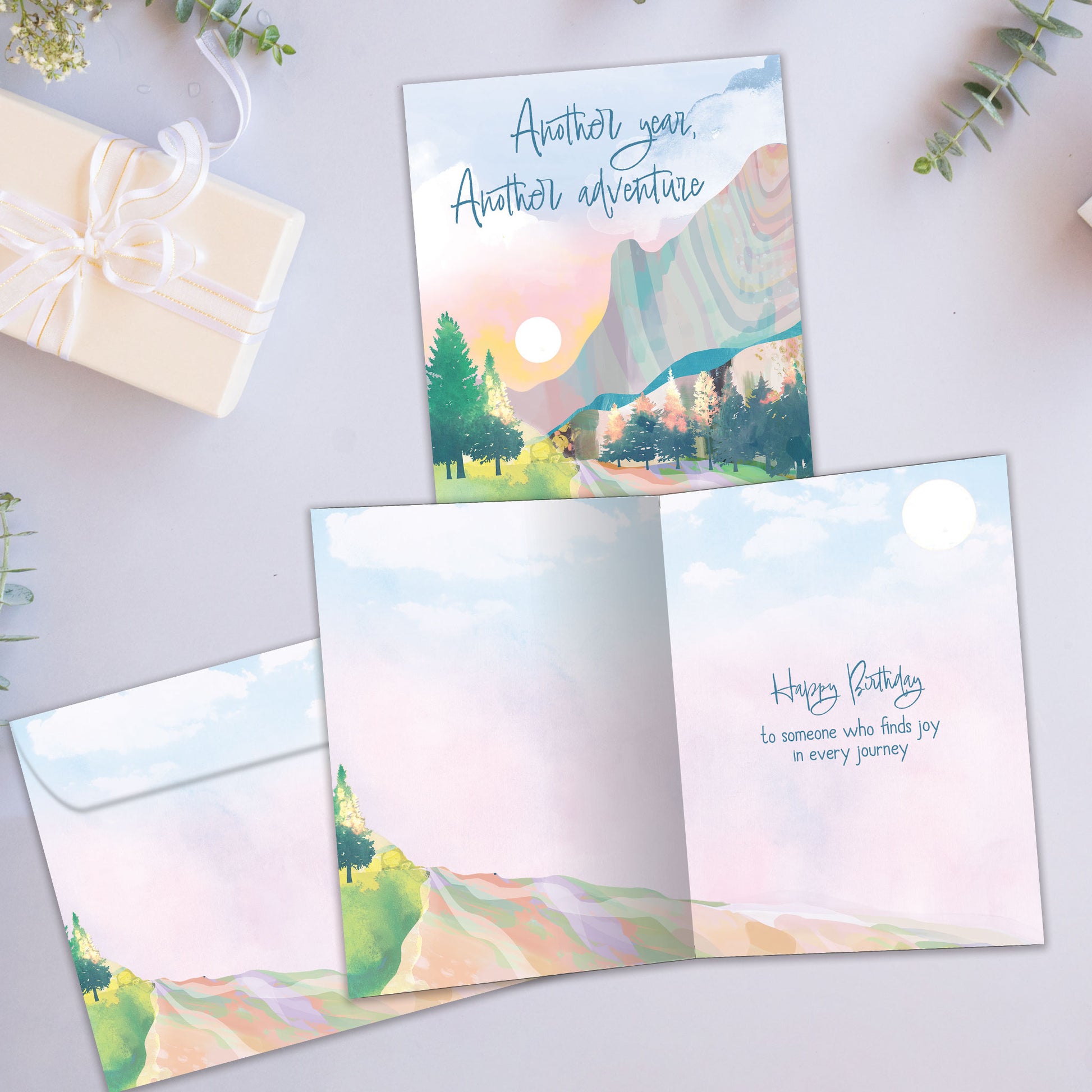 Front and inside view of a Birthday greeting card showcasing an illustration of a country road with the message "Another year, Another adventure," with a matching envelope.