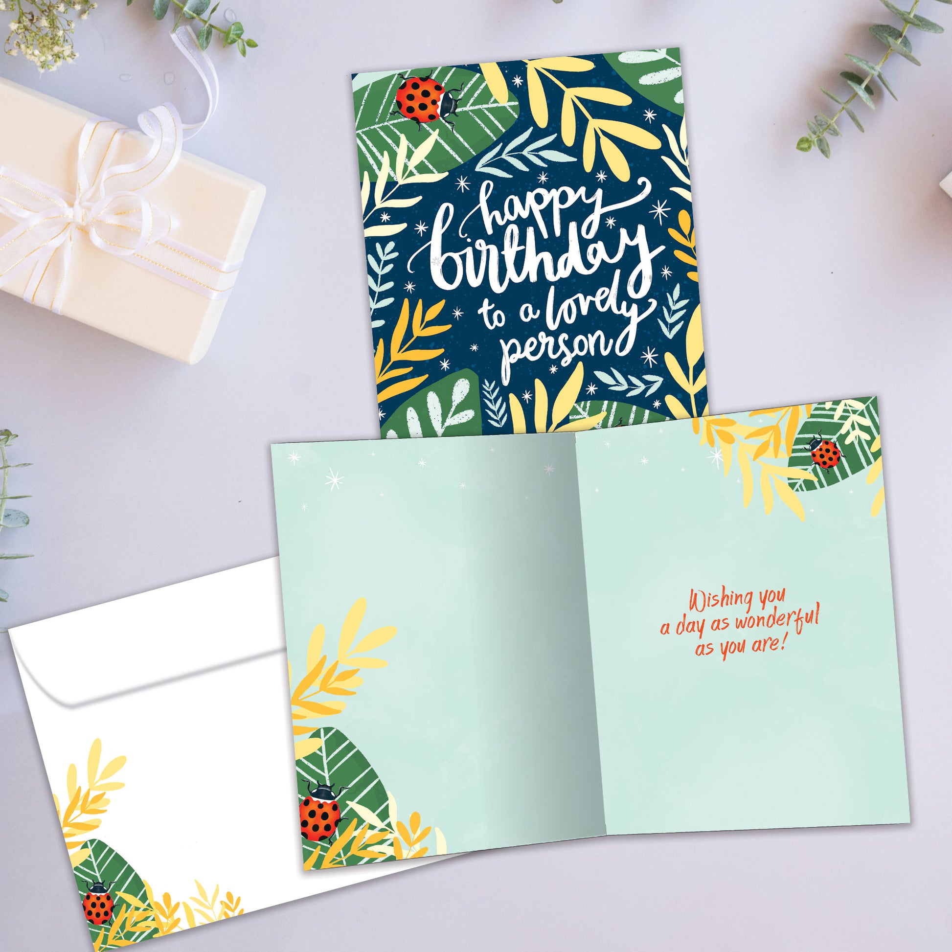 Front and inside view of a Birthday greeting card showcasing foliage and ladybugs surrounding a Happy Birthday message, with a matching envelope.