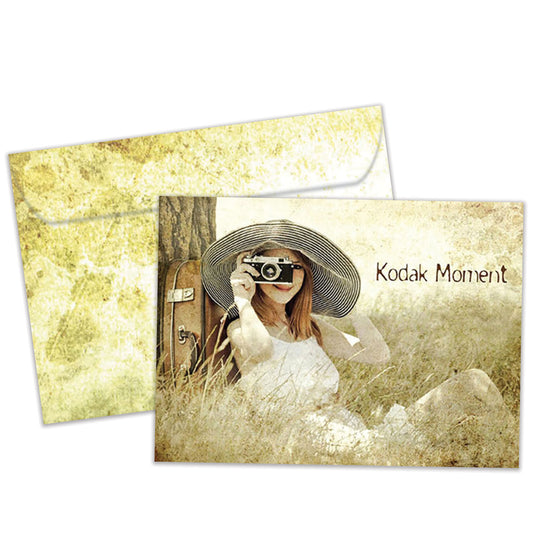 Front view of a Birthday greeting card featuring a woman sitting next to a tree taking a picture with the words "Kodak moment", with a matching envelope.